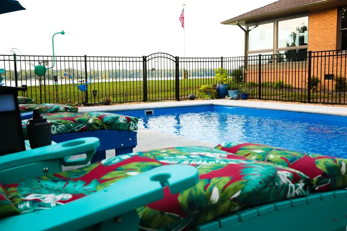 Outdoor pool with colorful inflatable rafts, black fence, and a covered patio in the background
