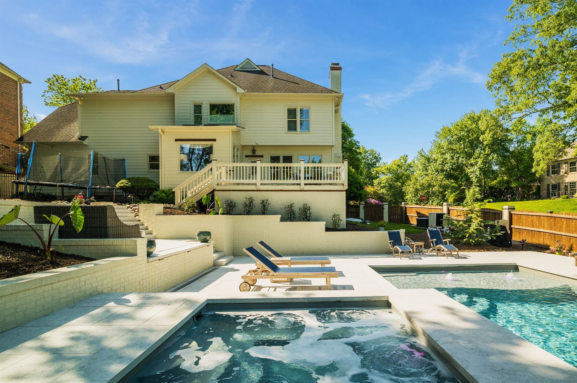 Backyard pool and hot tub behind a white two-story house on a sunny day