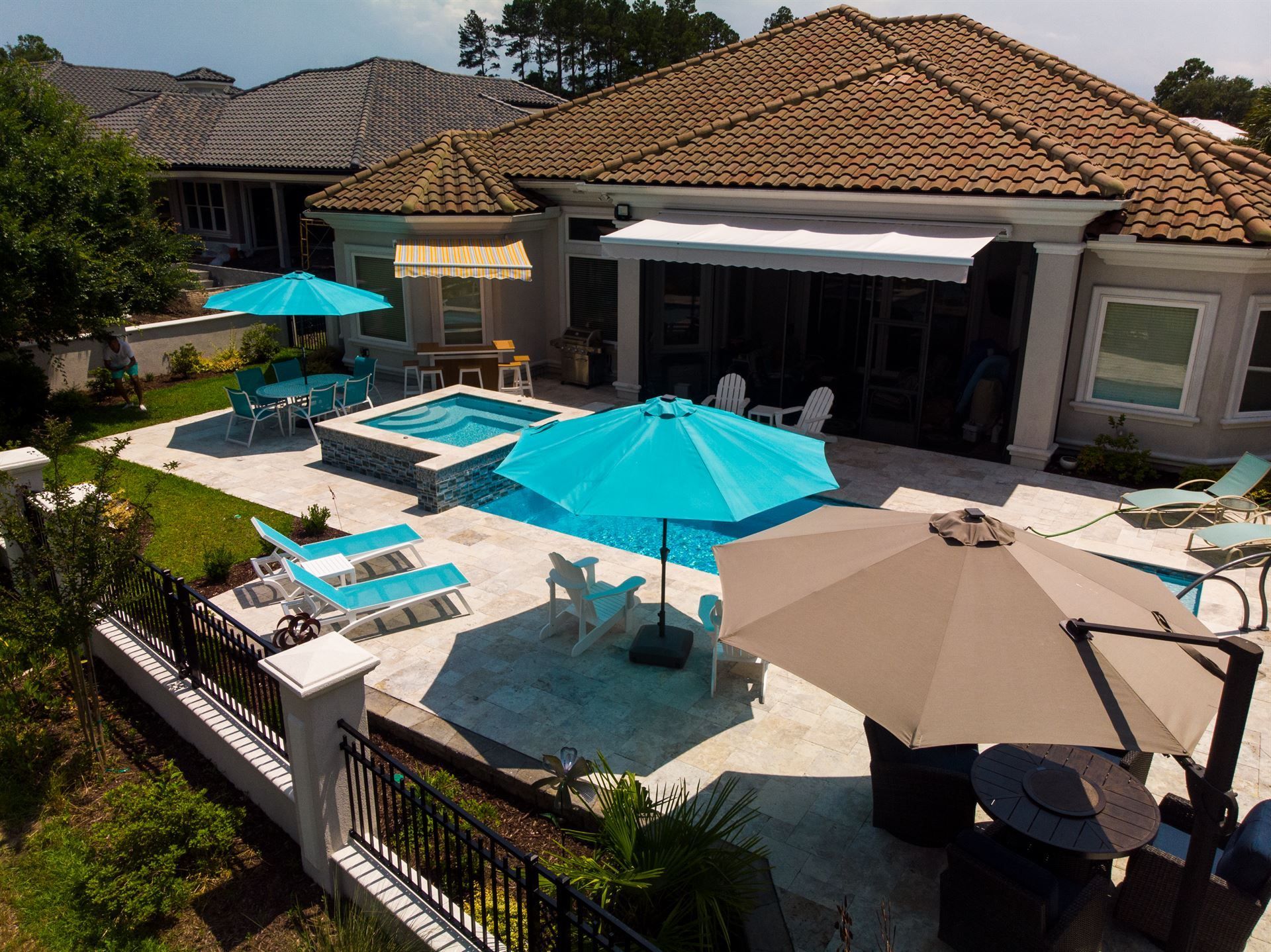 Sunny patio with turquoise umbrellas, lounge chairs, and a swimming pool beside a tiled house