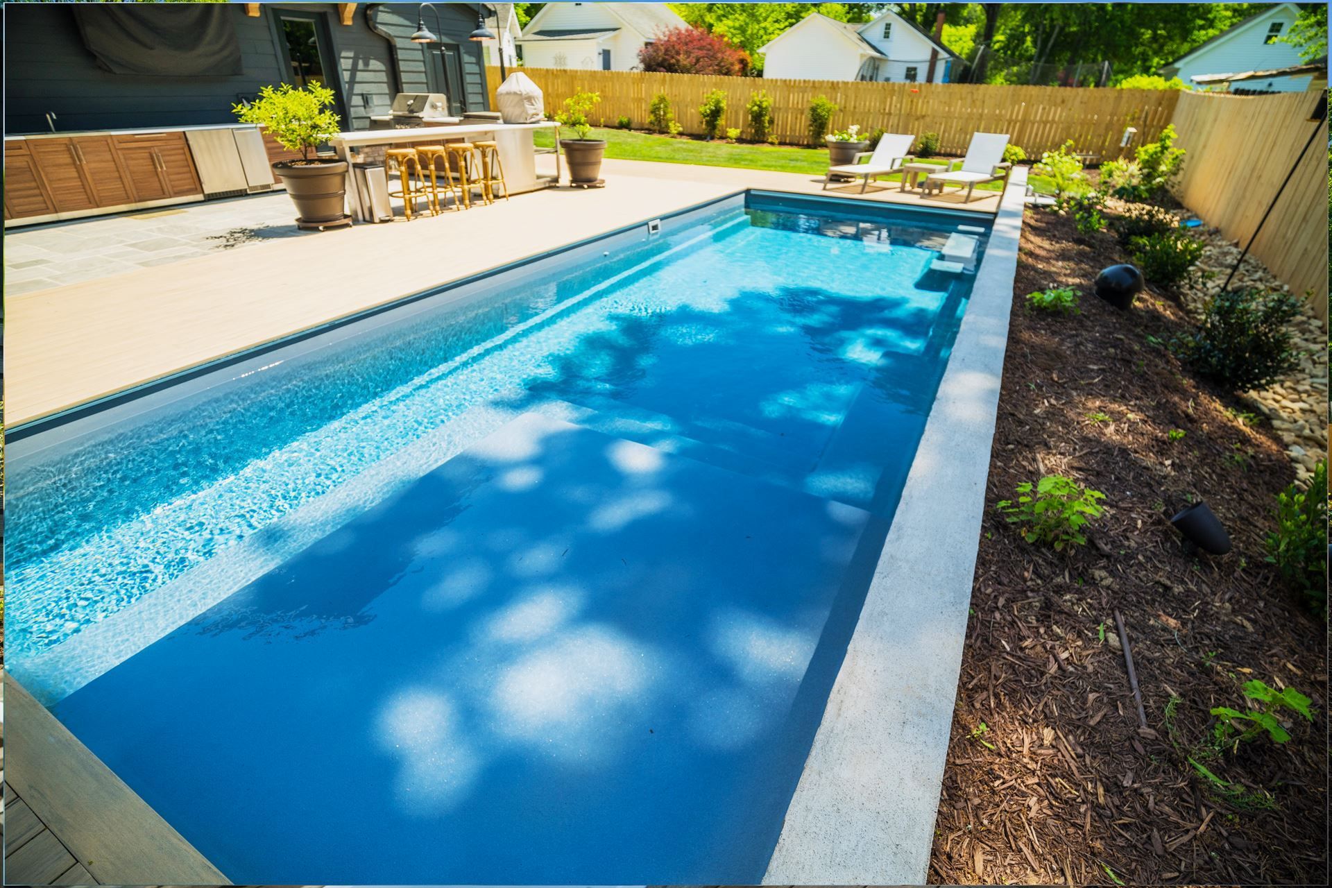 Backyard swimming pool with bright blue water and lounge chairs beside it