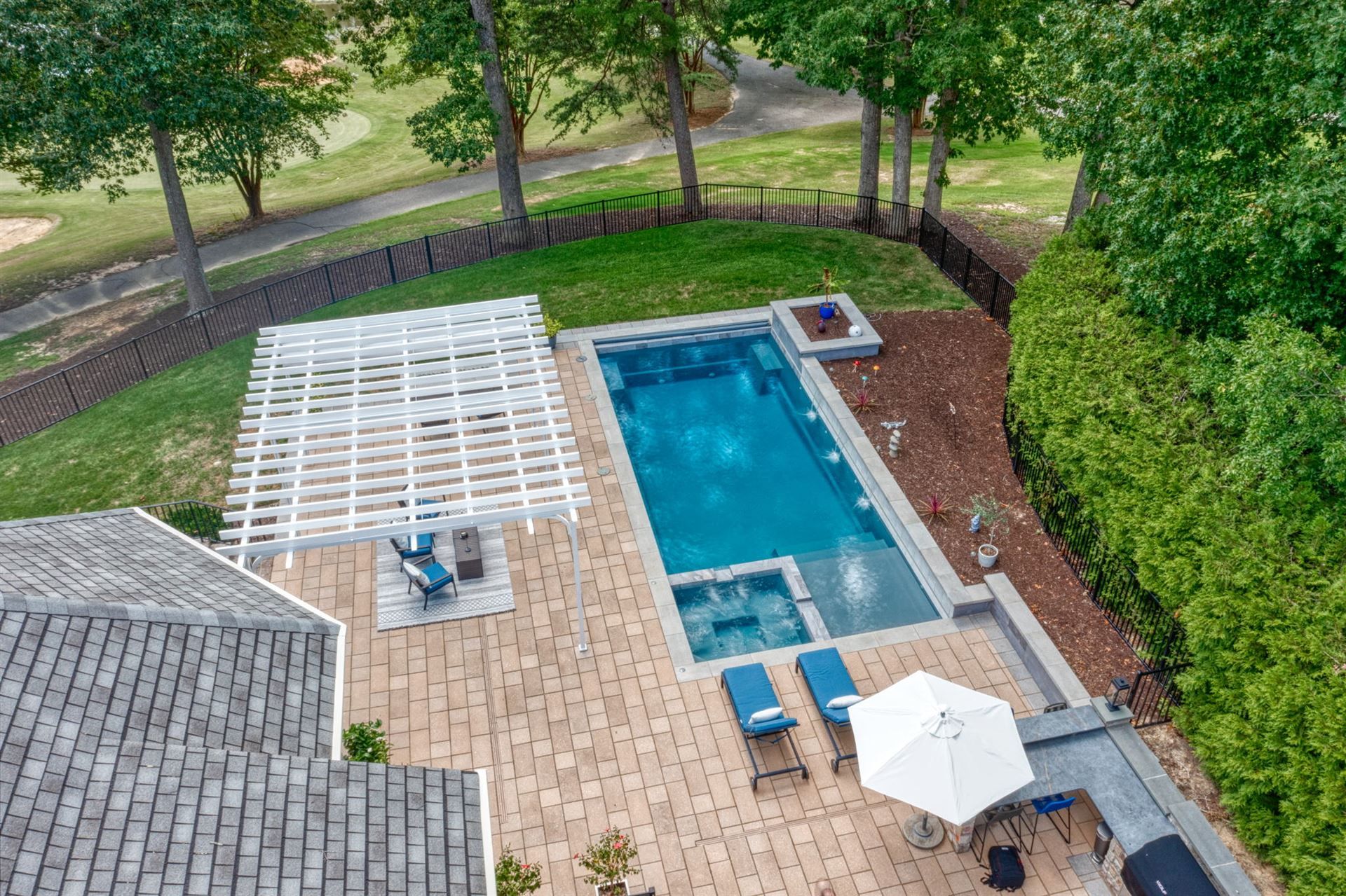 Overhead view of a backyard pool patio with lounge chairs, umbrellas, and surrounding trees.