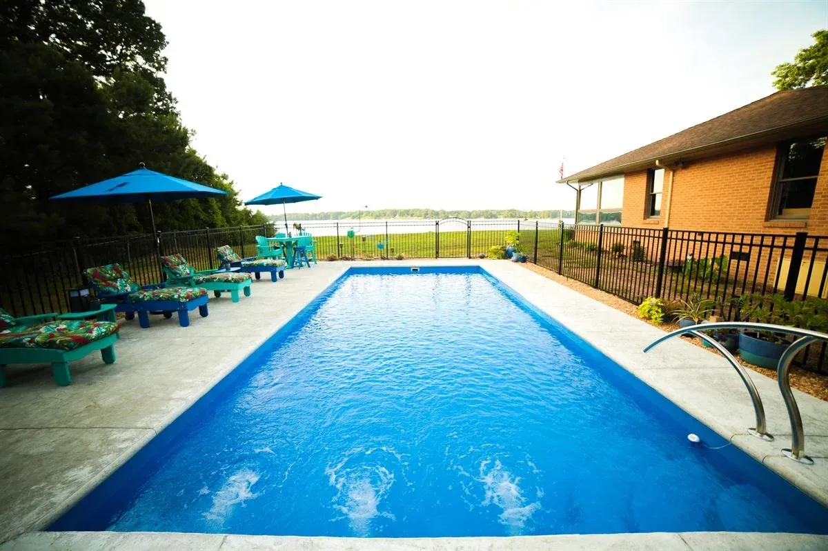 Outdoor swimming pool with blue water, lounge chairs, umbrellas, and a patio beside a building