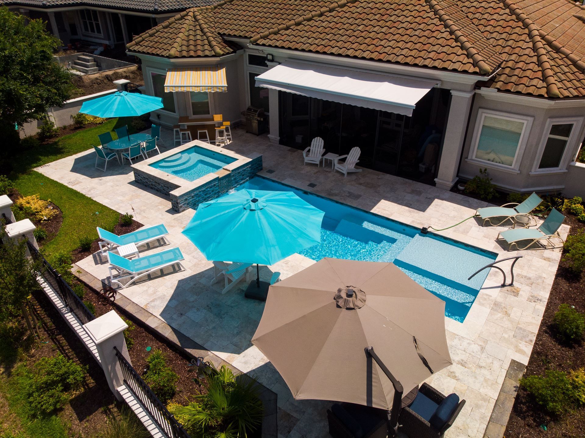 Backyard patio with a turquoise pool, hot tub, and large beige umbrella beside a house