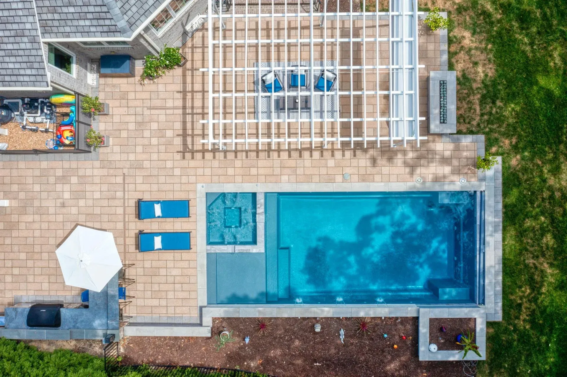 Overhead view of a backyard patio with a rectangular swimming pool, lounge chairs, umbrella, and potted plants