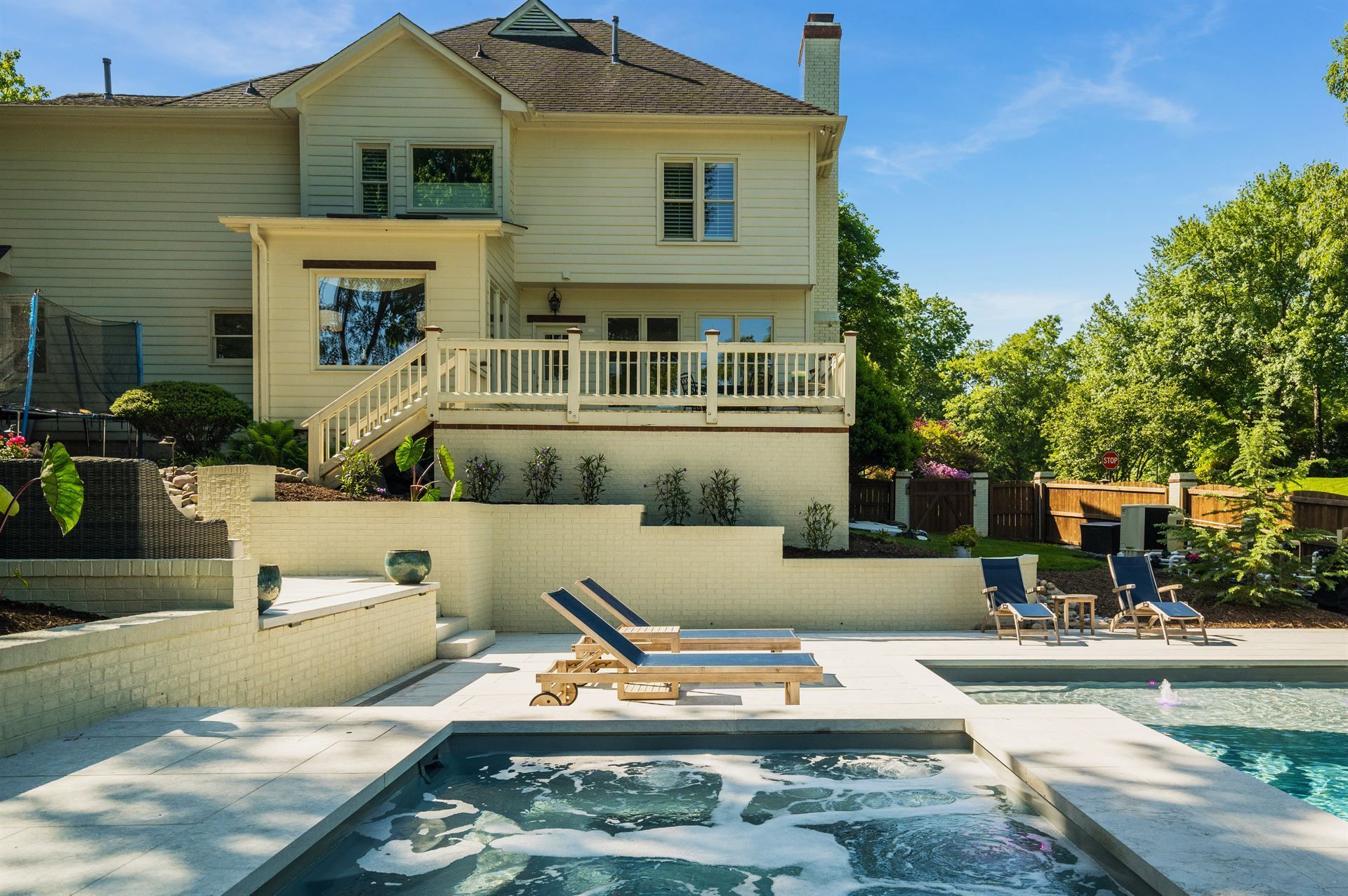 Backyard patio with a hot tub, lounge chairs, and a beige house with a deck