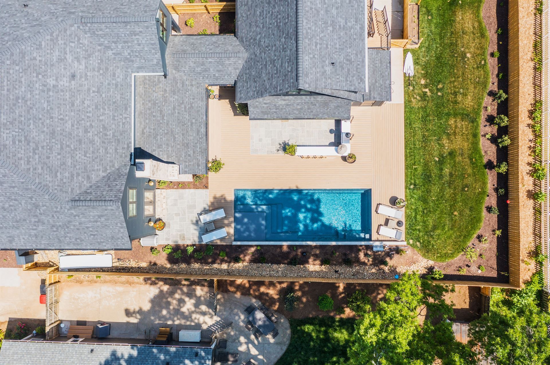 Aerial view of a modern backyard with a blue rectangular pool, patio seating, and surrounding greenery