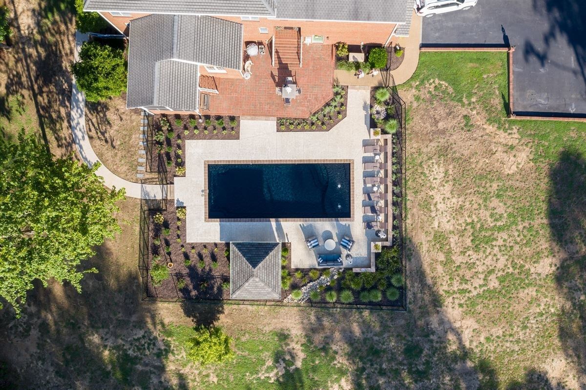Aerial view of a backyard with a swimming pool, patio seating, and surrounding lawn.