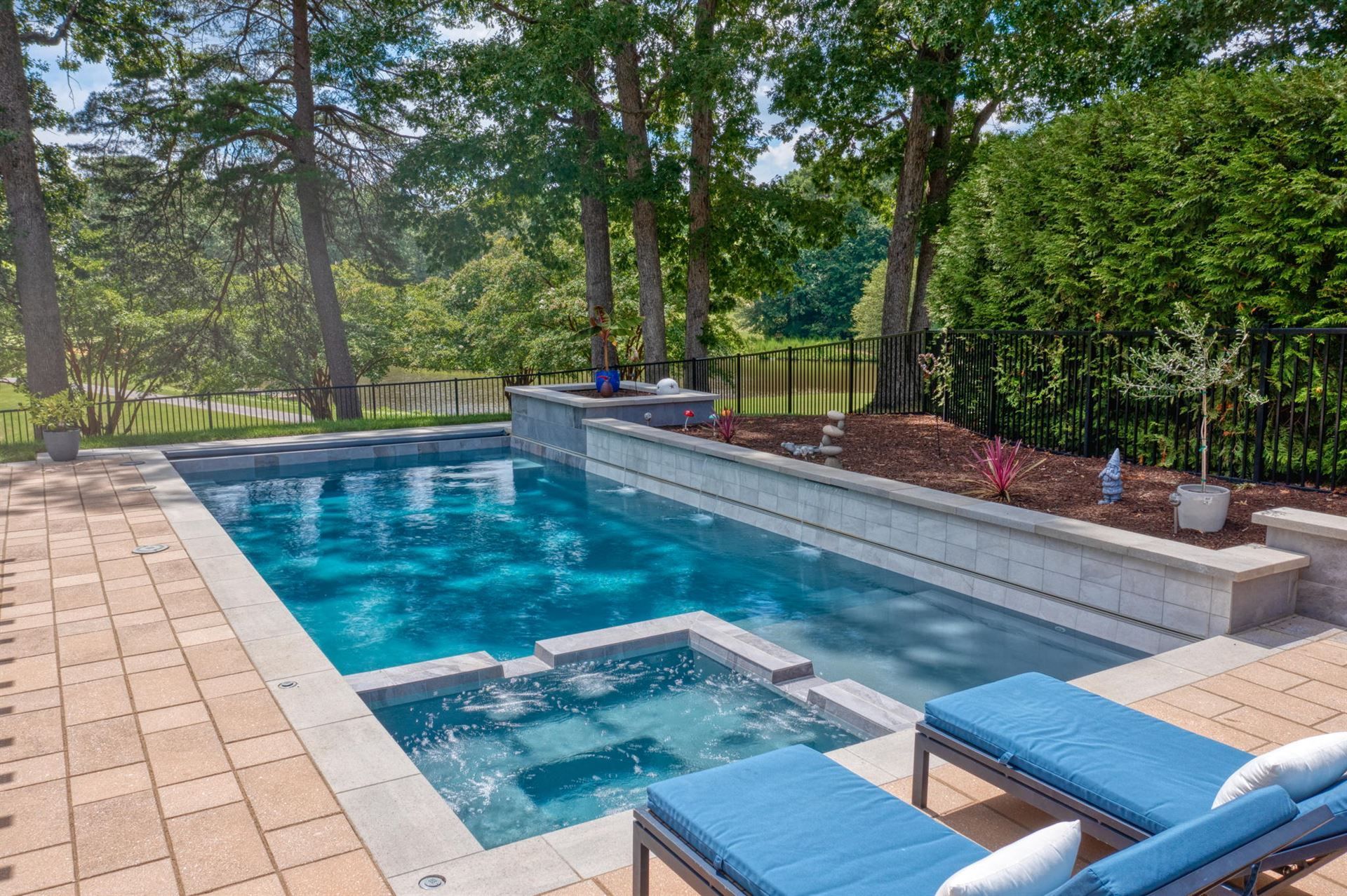 Backyard swimming pool with blue lounge chairs, stone patio, and trees beside a hedge