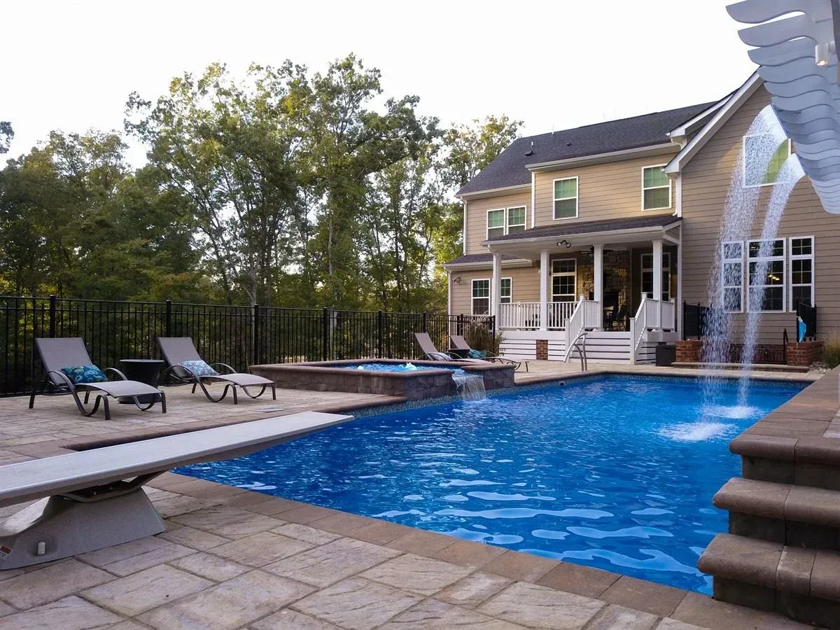 Backyard pool with lounge chairs and a two-story house beside a deck and trees