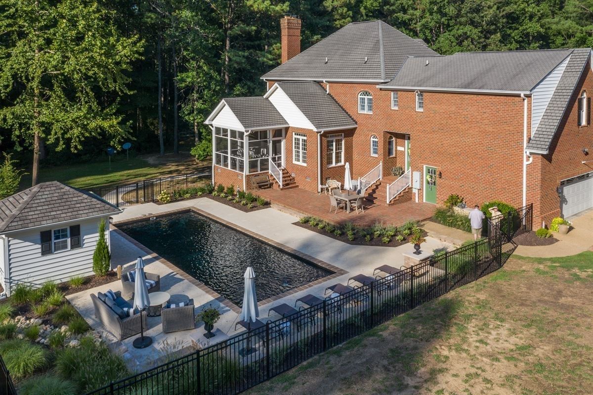 Aerial view of a brick house with a covered patio, pool, and fenced backyard.