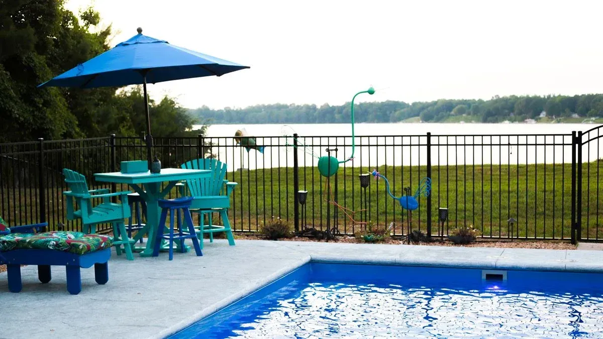 Blue patio umbrella and poolside seating beside a fenced waterfront deck with a pool in the foreground