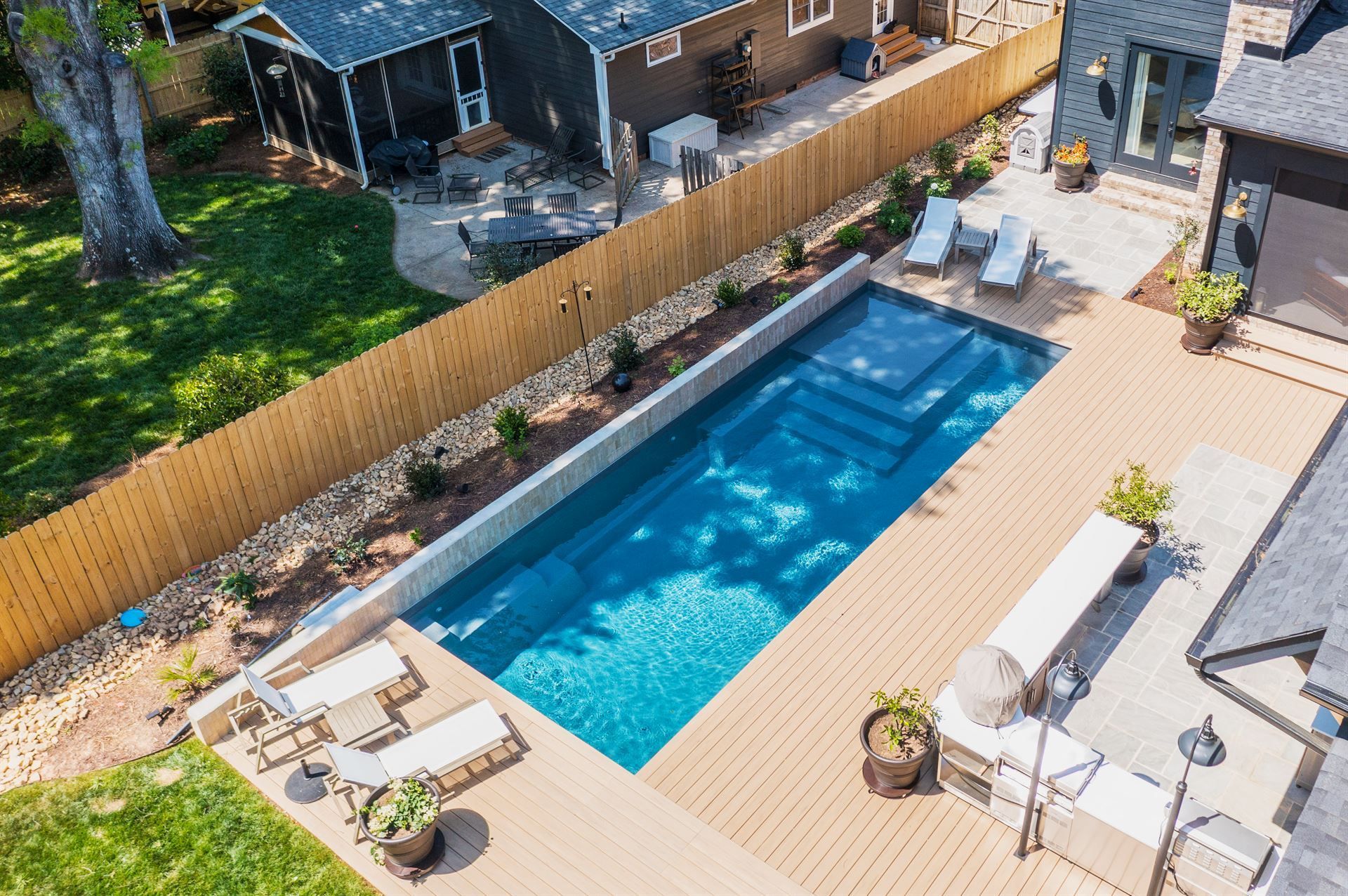 Backyard with a long blue swimming pool, wooden deck, lounge chairs, and patio furniture.