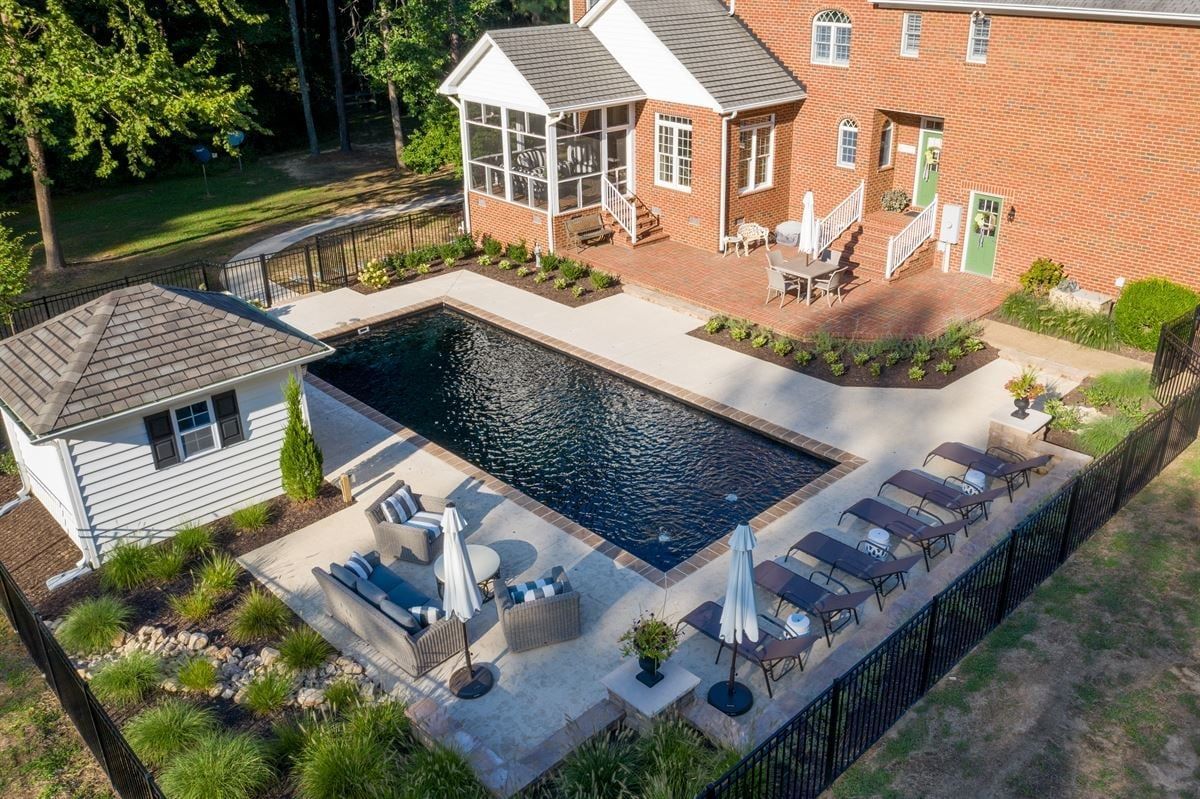 Backyard pool with patio seating, umbrellas, and a brick house beside a small pavilion
