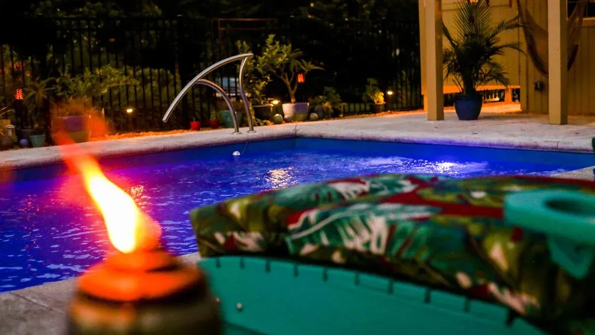 Lit poolside patio at night with flaming torch and lounge chair in foreground