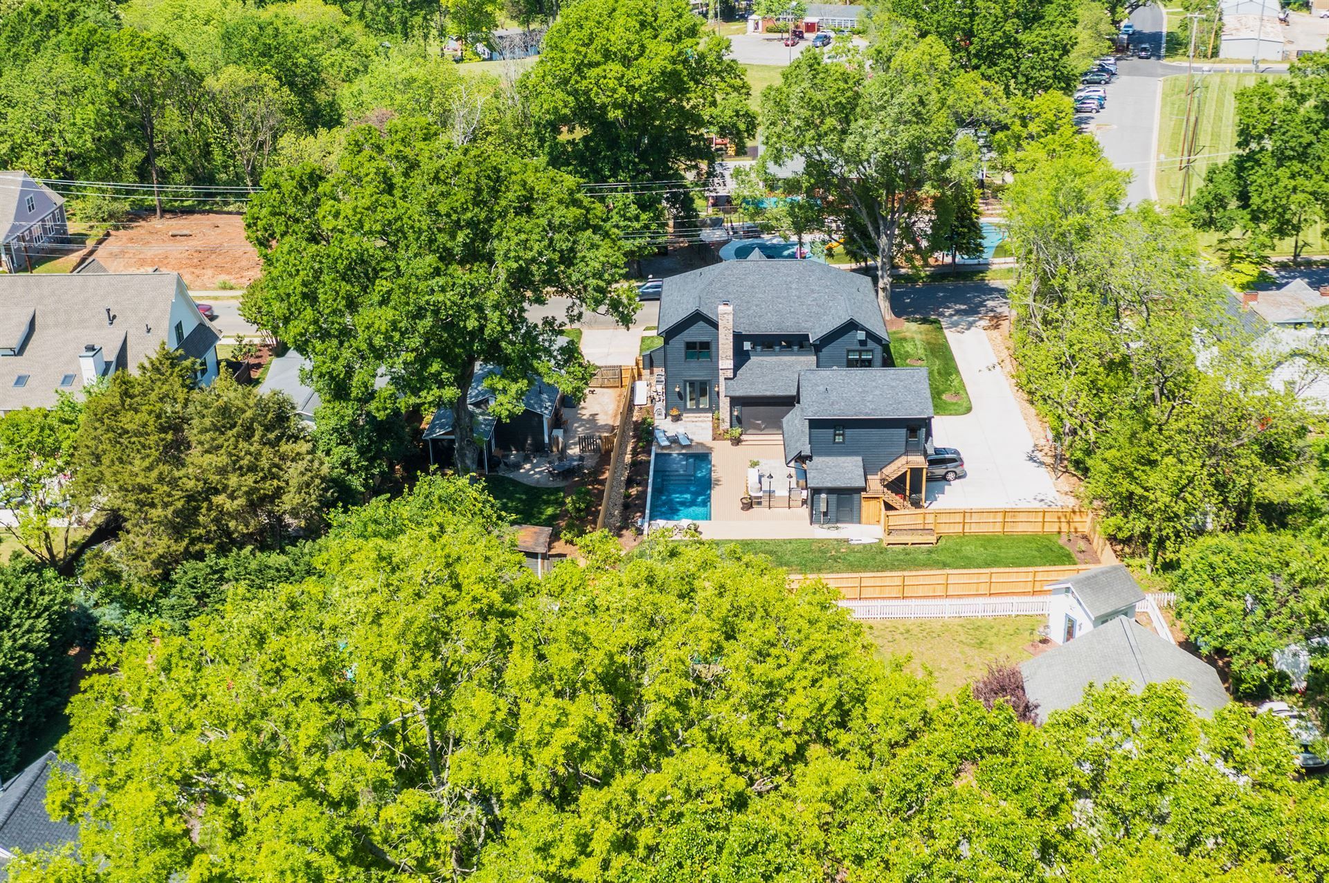 Aerial view of a house with a backyard pool surrounded by lush green trees and neighboring homes