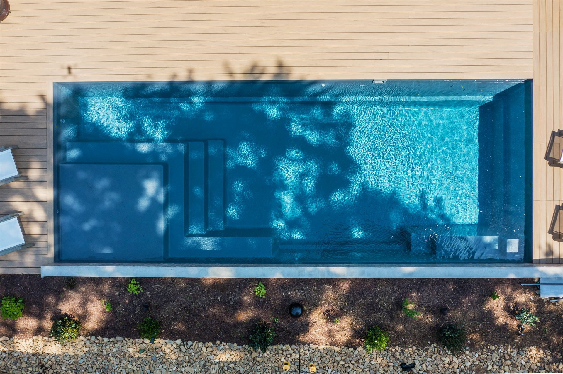 Rectangular blue backyard pool beside a wooden deck, viewed from above