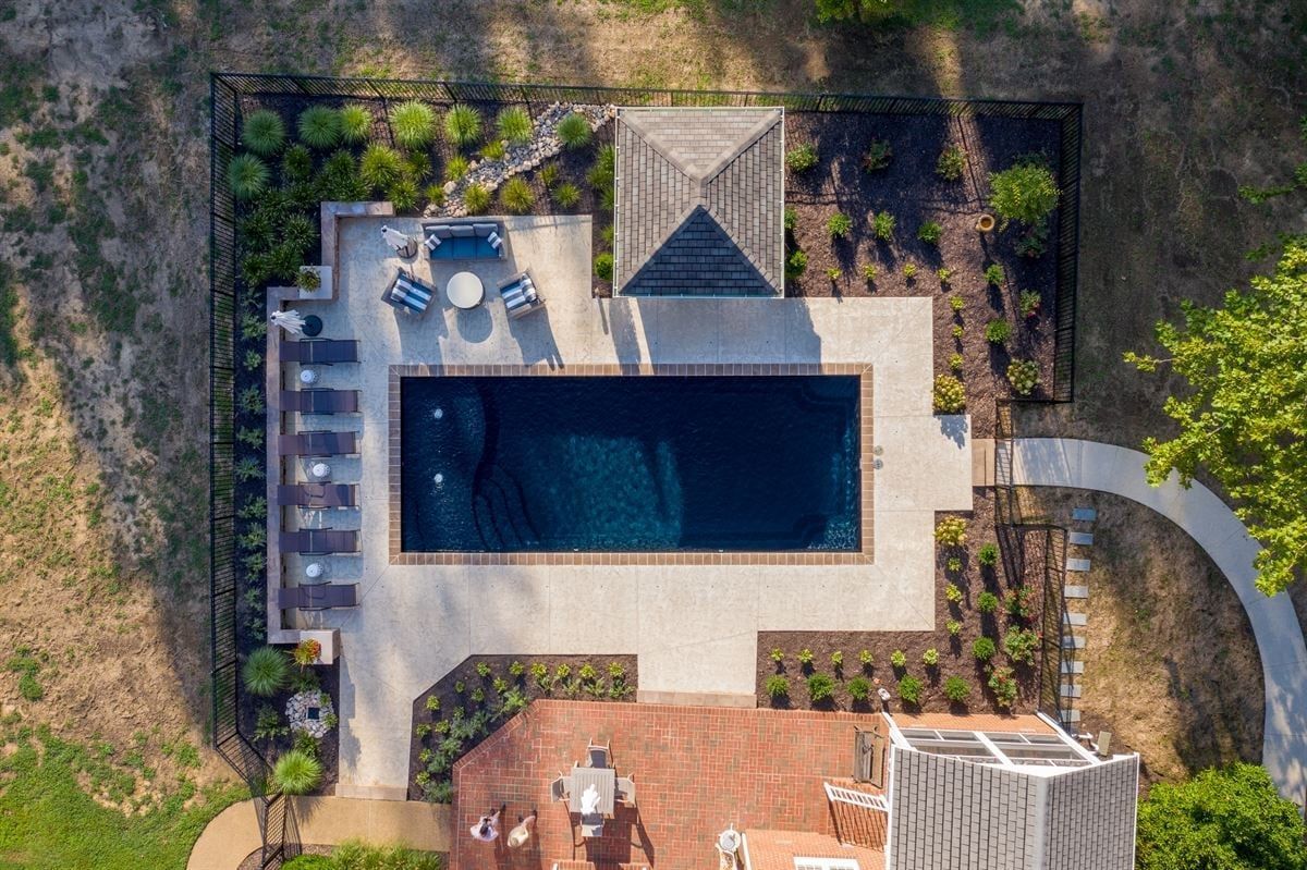 Overhead view of a backyard pool with lounge chairs, patio seating, and surrounding landscaping
