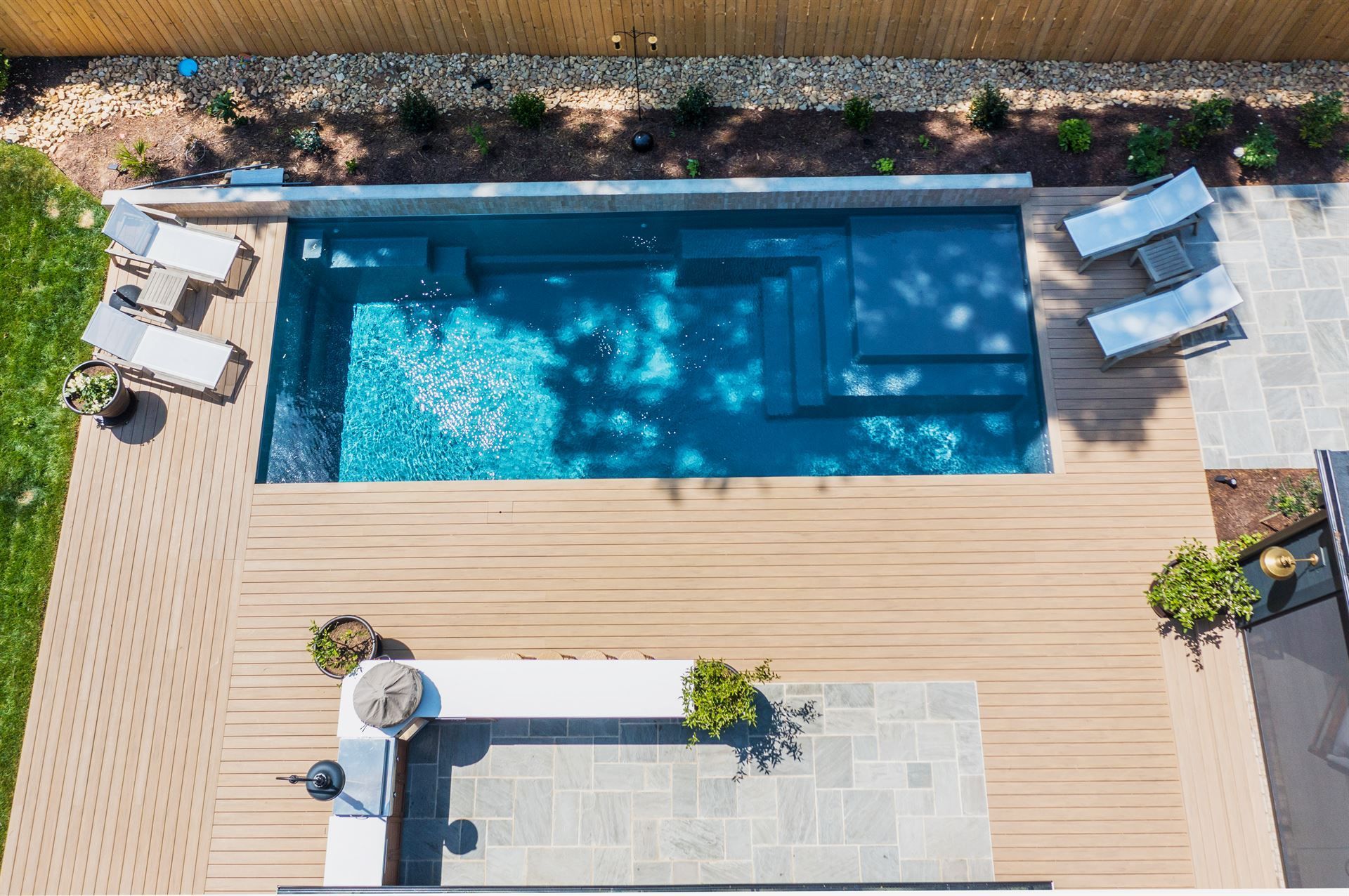 Aerial view of a backyard with a rectangular swimming pool, wood deck, and lounge chairs.