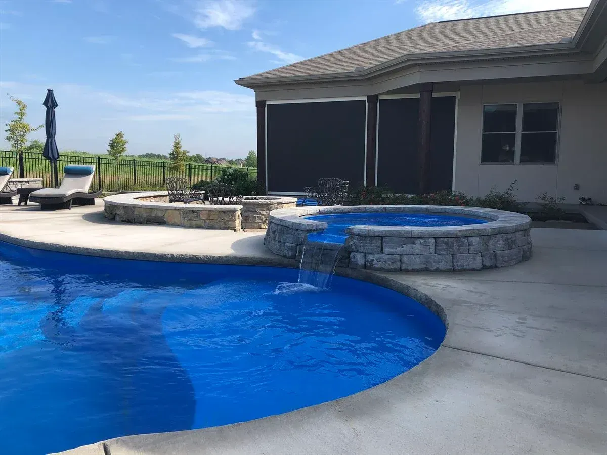 Backyard pool with stone spa, patio seating, and covered patio under a blue sky