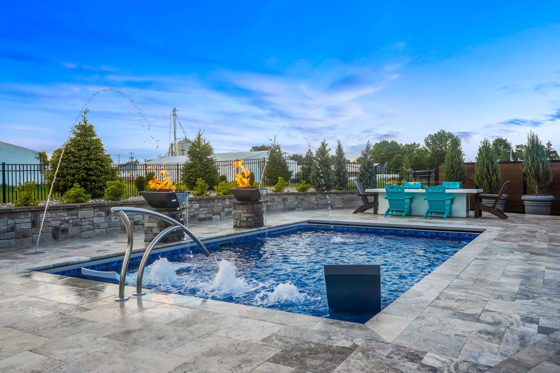 Outdoor patio with a bubbling blue hot tub, stone deck, and lounge seating under a bright sky