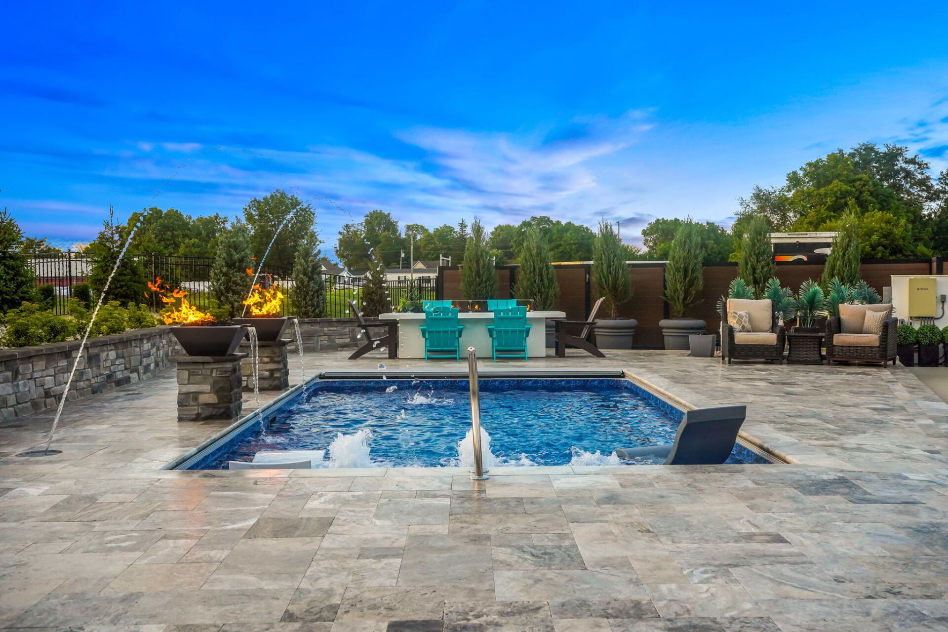 Outdoor patio with a small square pool, blue chairs, stone paving, and landscaped seating area at dusk