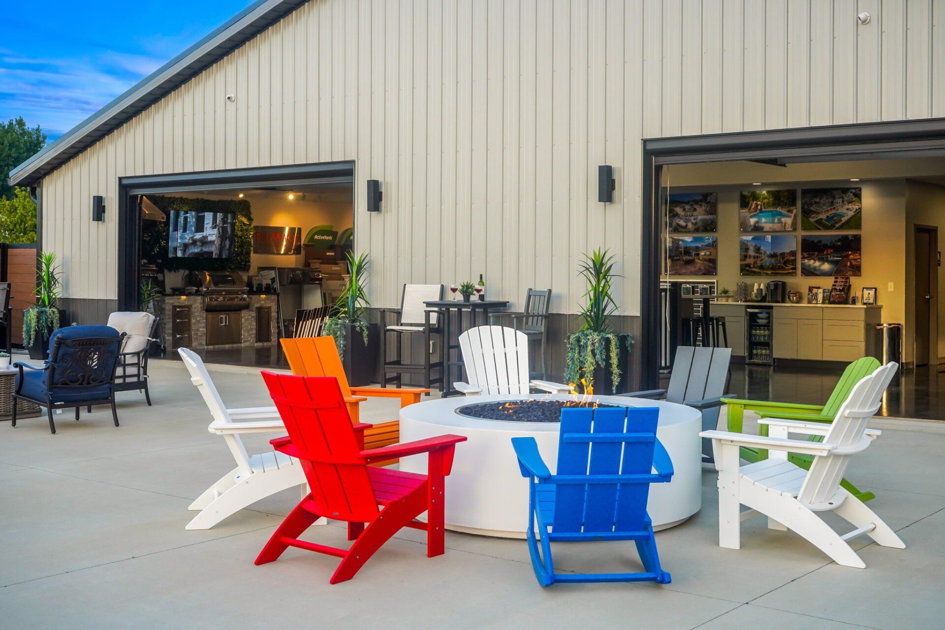 Colorful Adirondack chairs around a white table on a patio outside a beige building