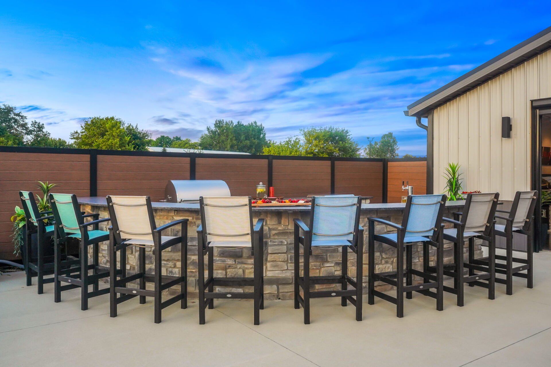 Outdoor patio with two long dining tables, black chairs, and a beige building under a blue sky