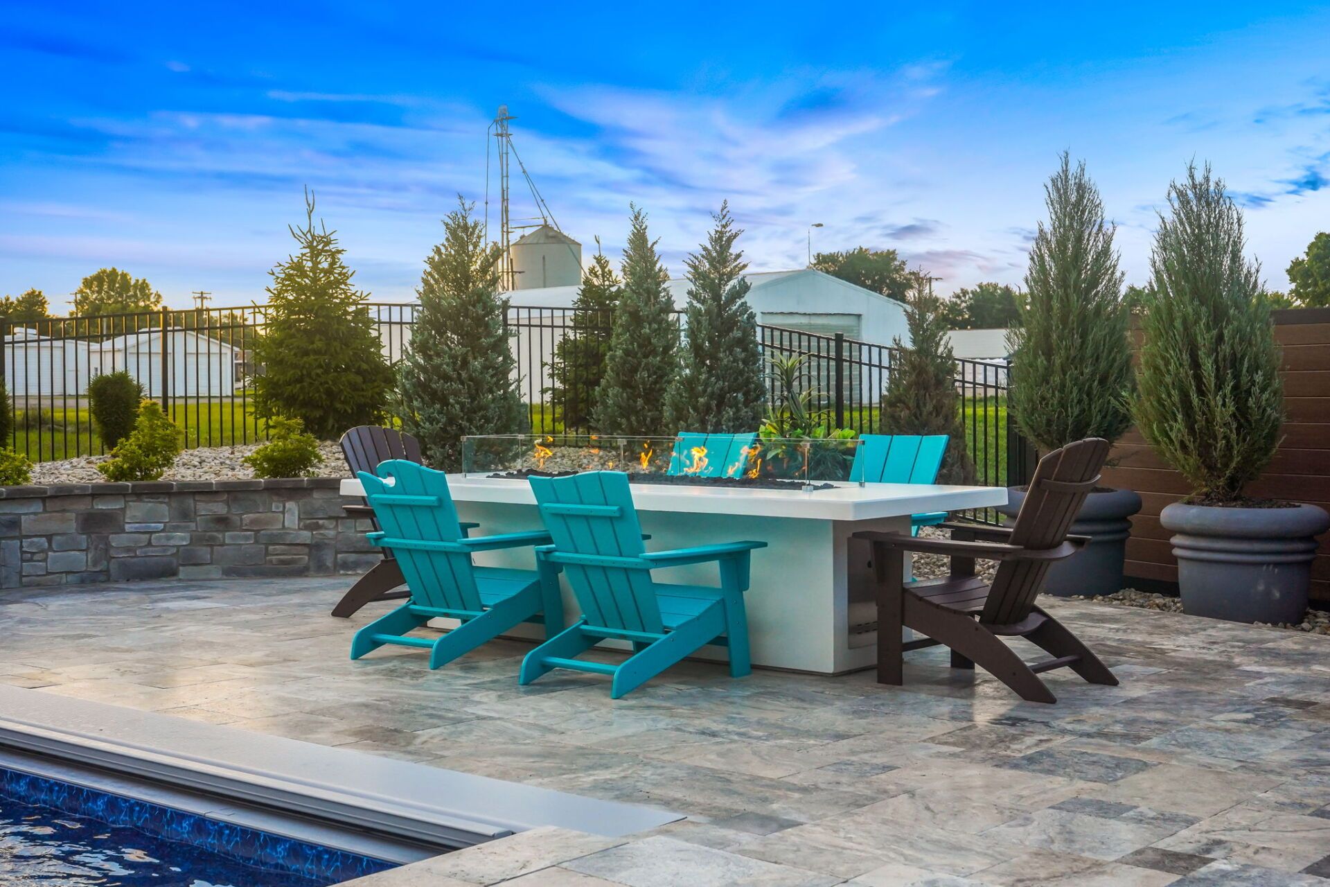 Backyard patio with turquoise lounge chairs around a fire pit beside a pool at sunset