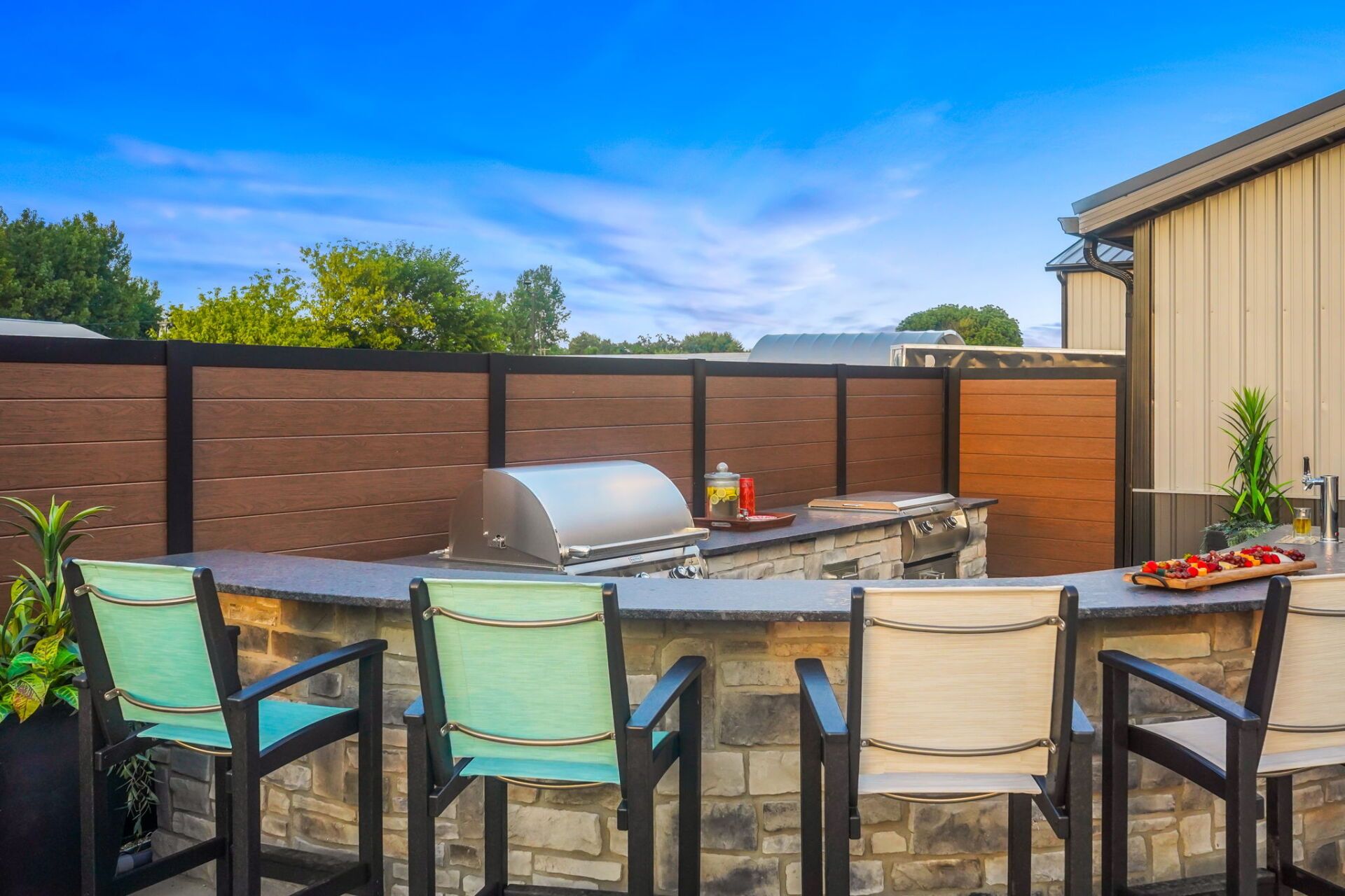 Backyard patio with stone table, four chairs, grill, and brown privacy fence under blue sky