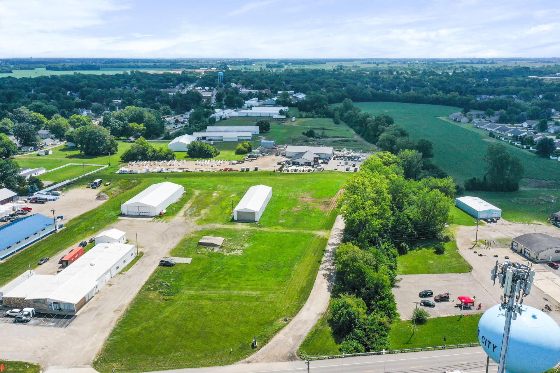 Aerial view of a rural fairground with green fields, white tents, and parked vehicles on a sunny day