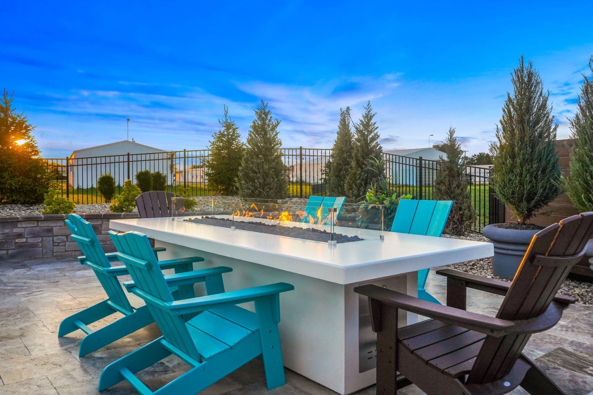 Outdoor patio with a long white dining table, turquoise chairs, and a fire pit at sunset