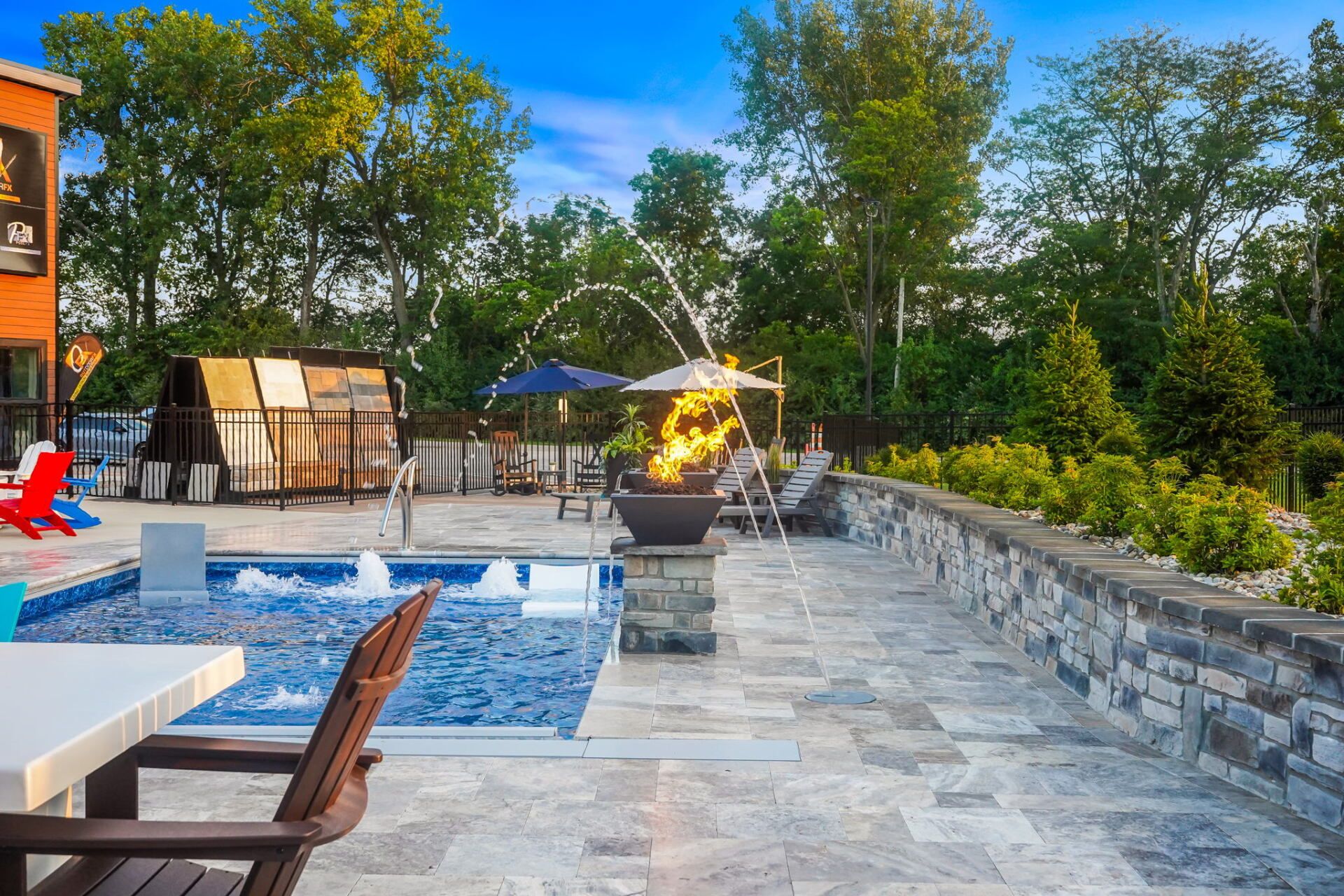 Resort pool with stone patio, lounge chairs, umbrellas, and a fire pit surrounded by trees