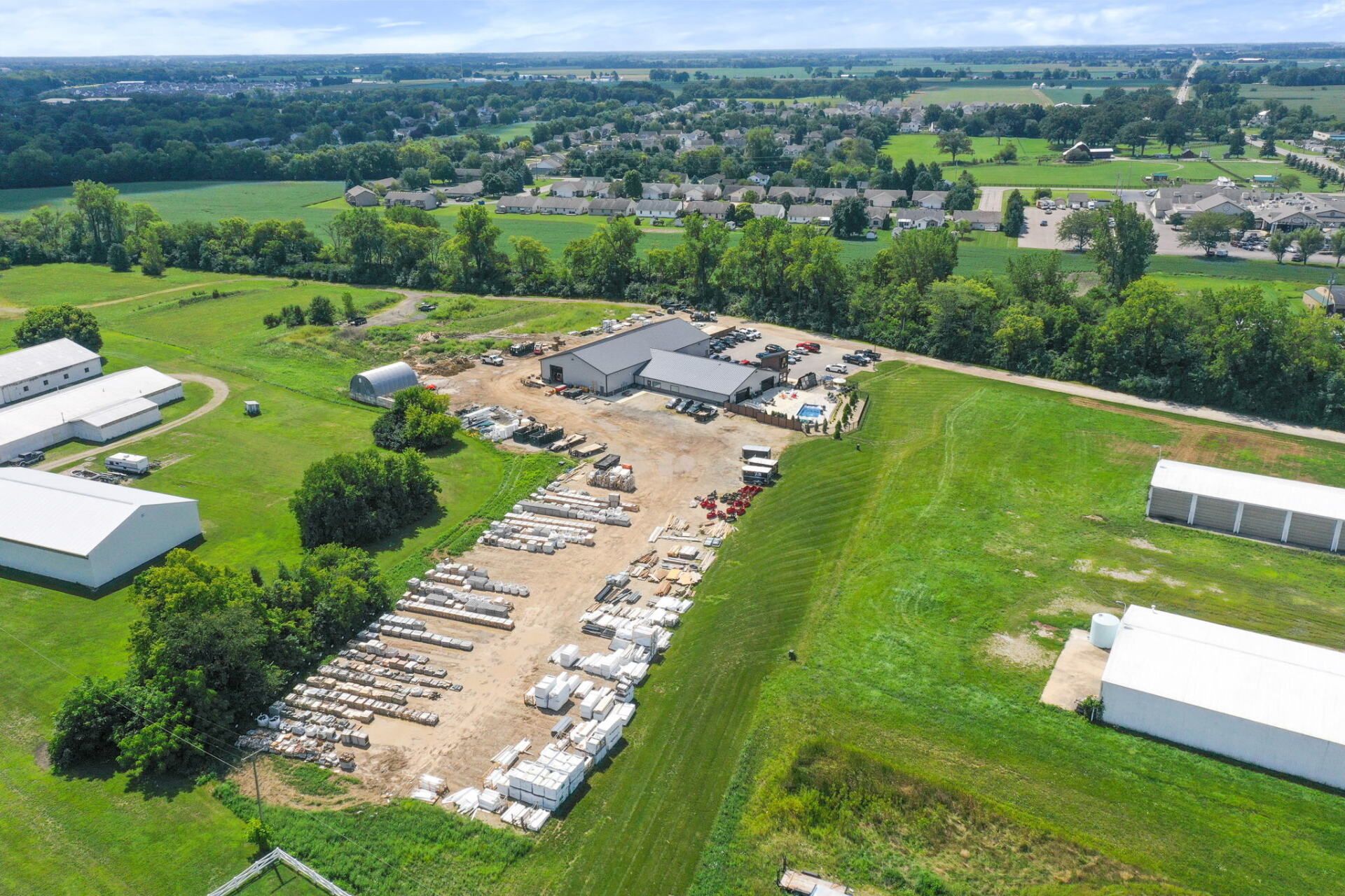 Aerial view of a rural construction site with buildings, materials, and green fields.