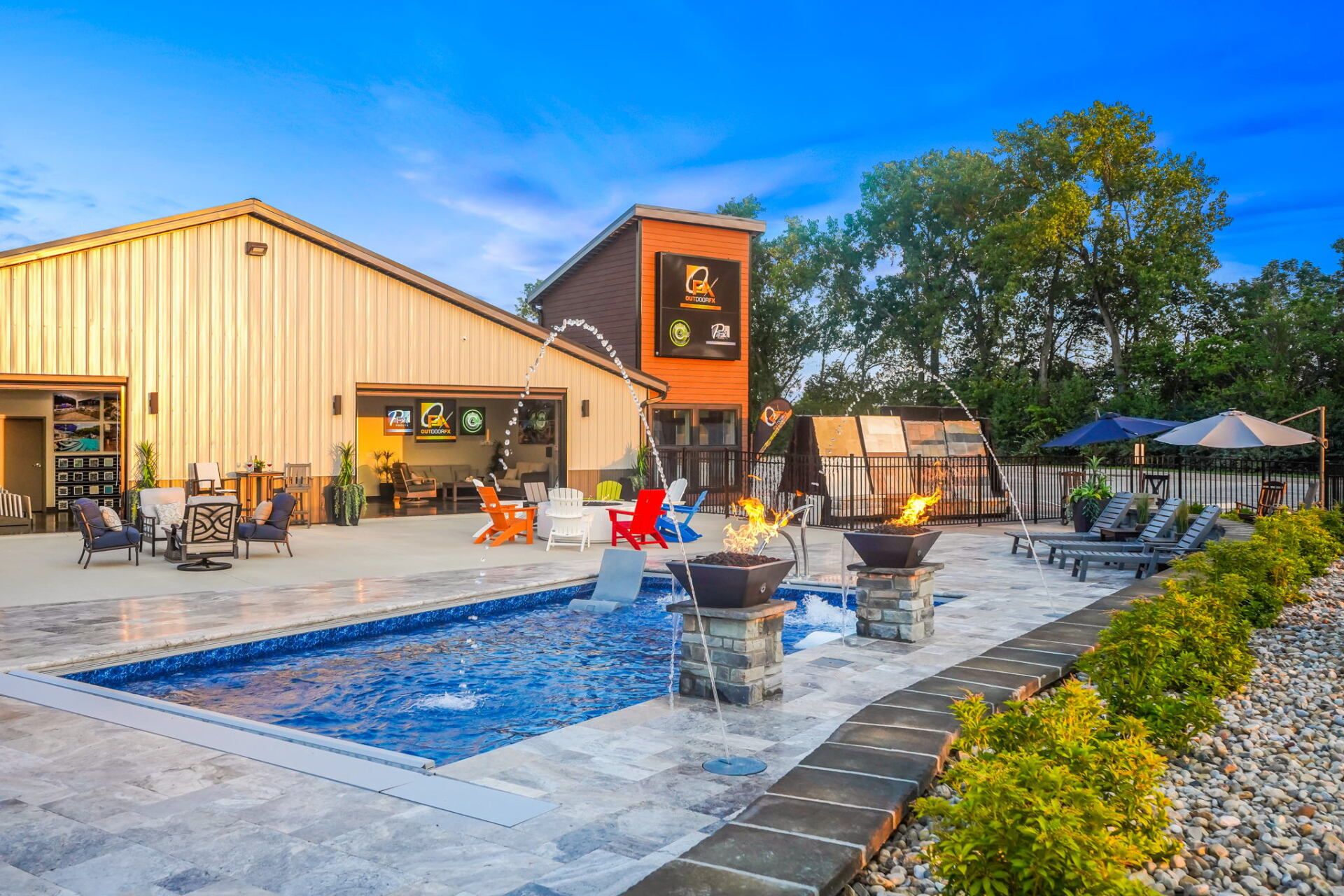 Outdoor patio with a long pool, lounge chairs, umbrellas, and a building under a blue sky