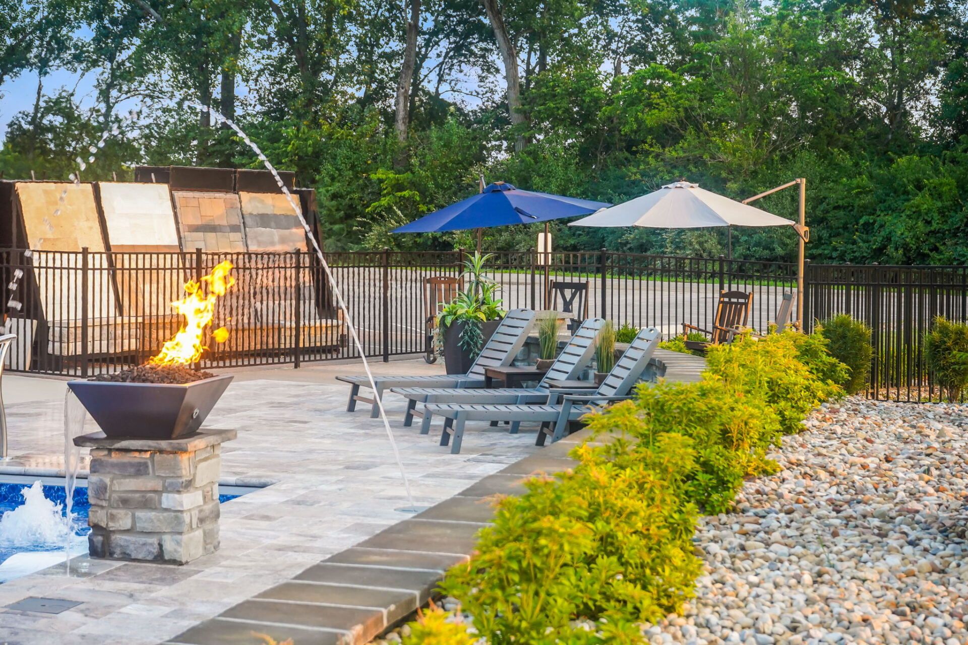 Outdoor patio with fire pit, lounge chairs, umbrellas, and a landscaped rock border at sunset