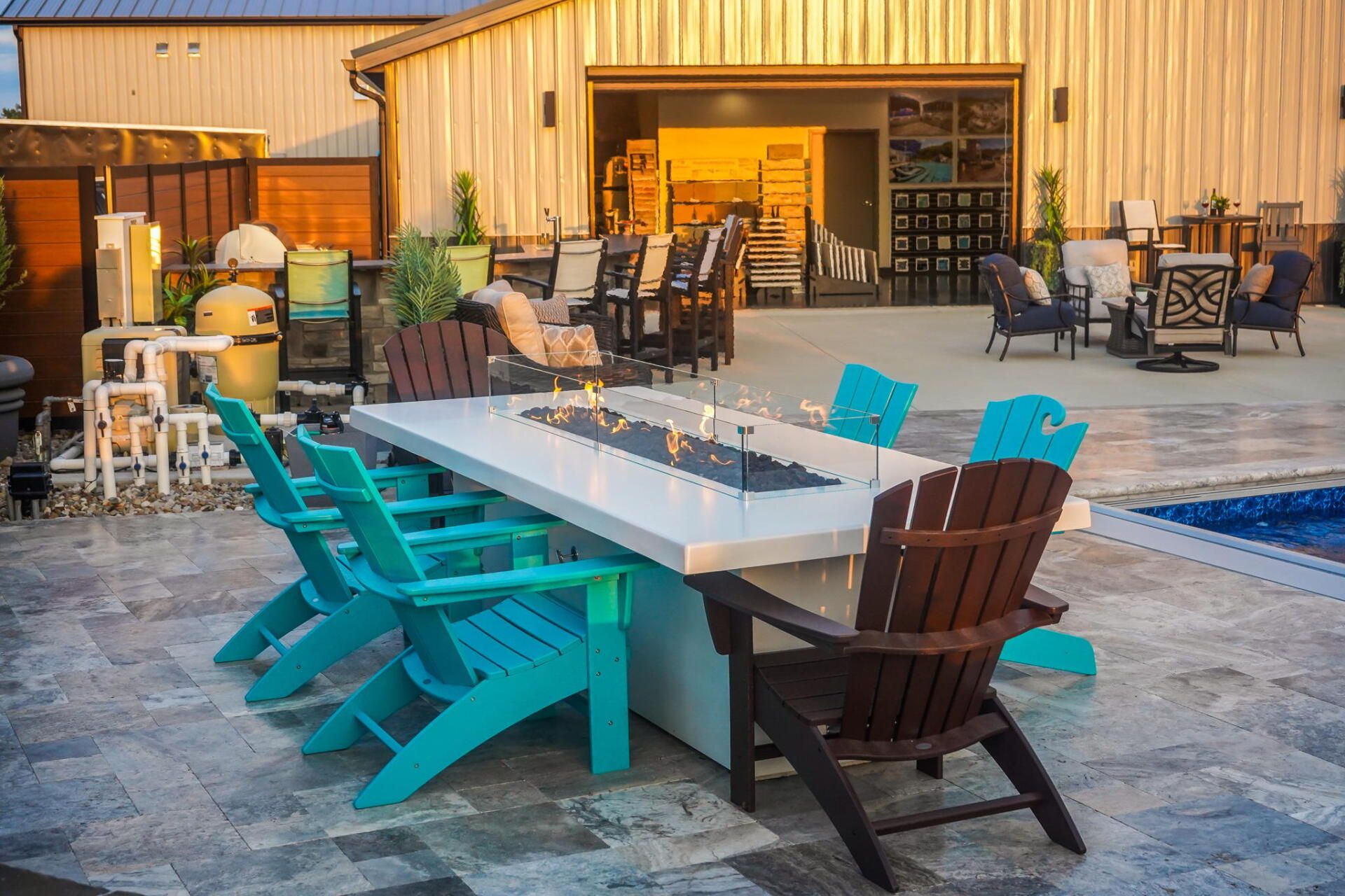 Outdoor patio with a long white table, turquoise chairs, and a brown chair beside a pool at sunset
