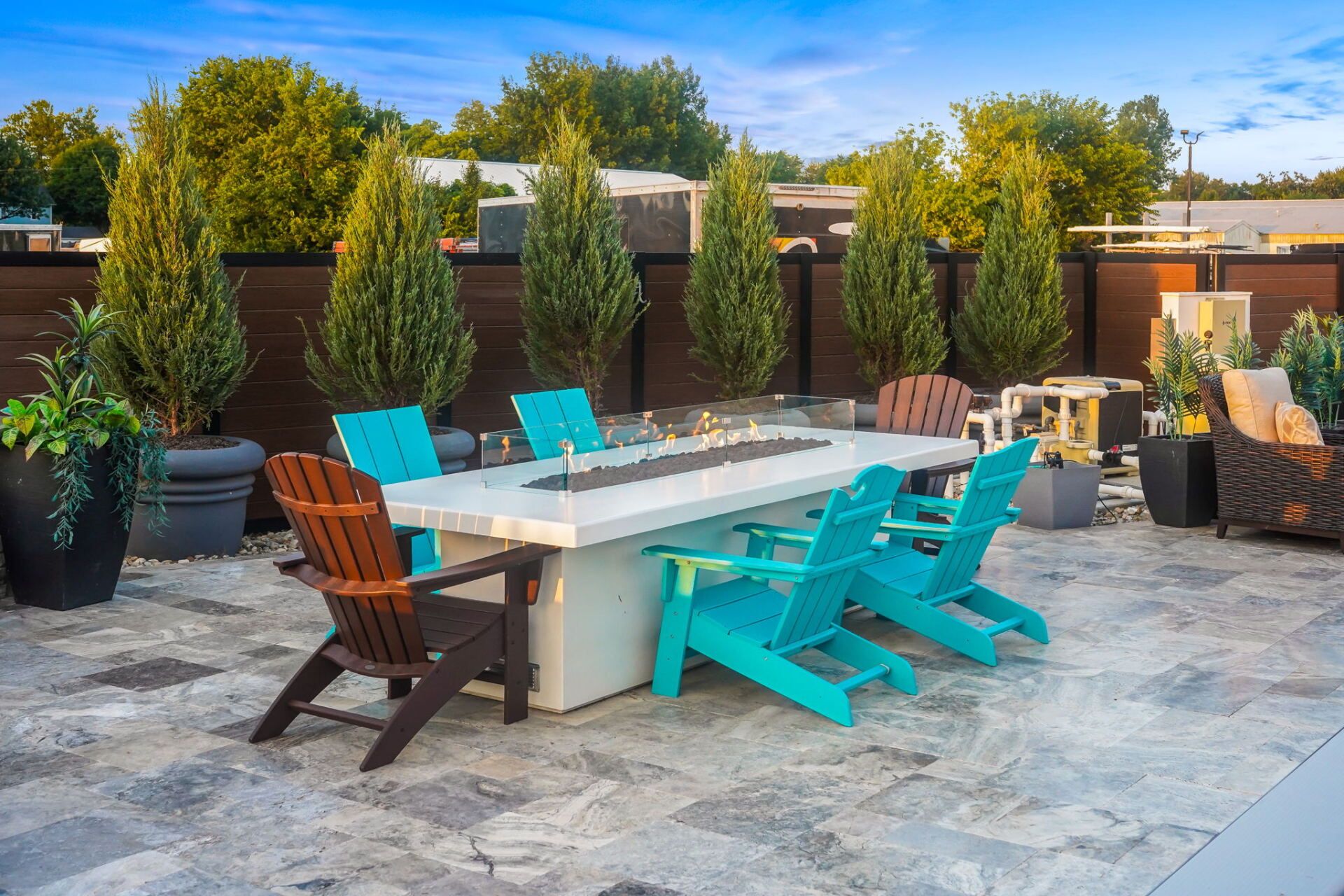 Outdoor patio with white dining table, turquoise chairs, and potted trees on a stone terrace