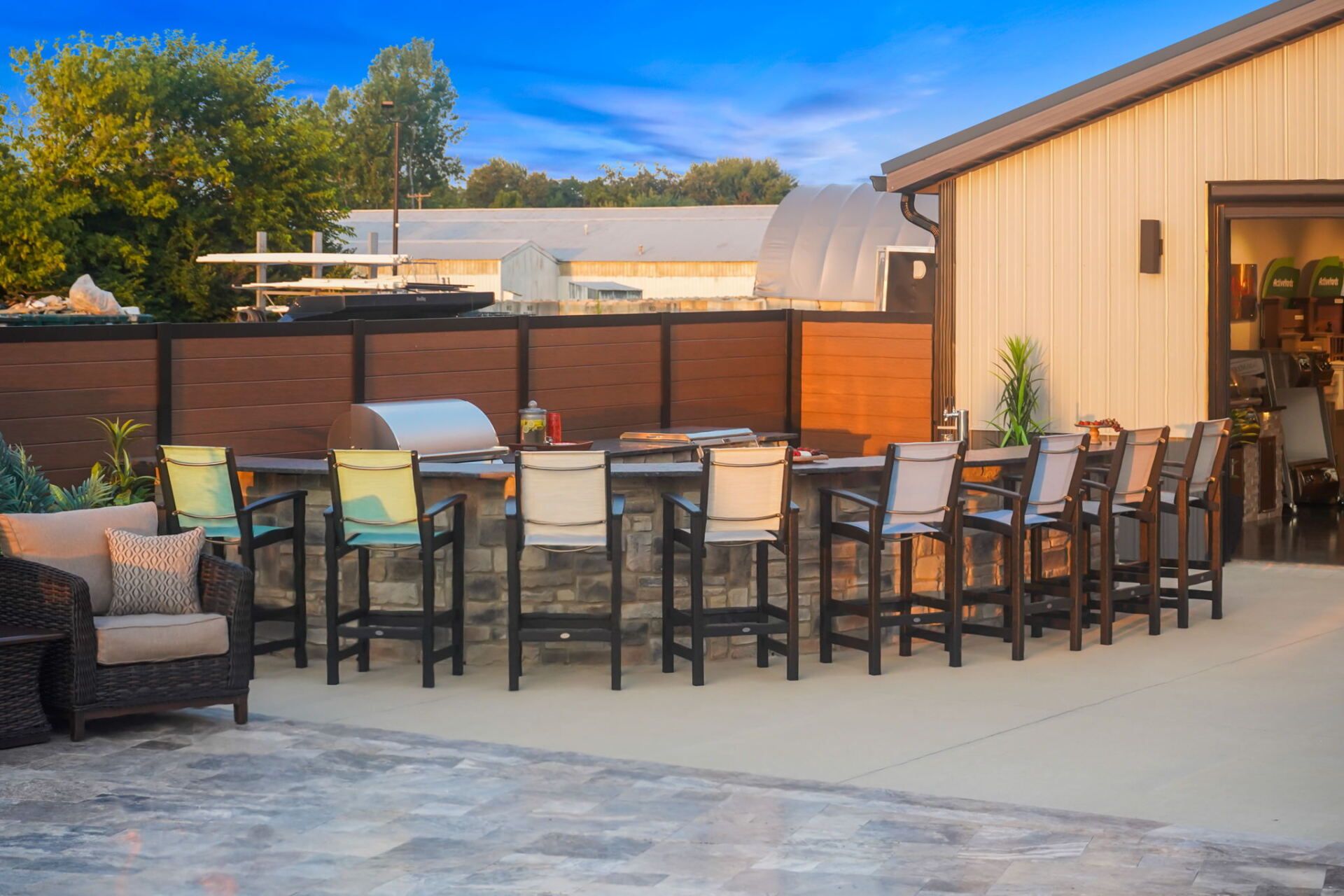 Outdoor patio with long dining table, chairs, and lounge seating beside a building at sunset