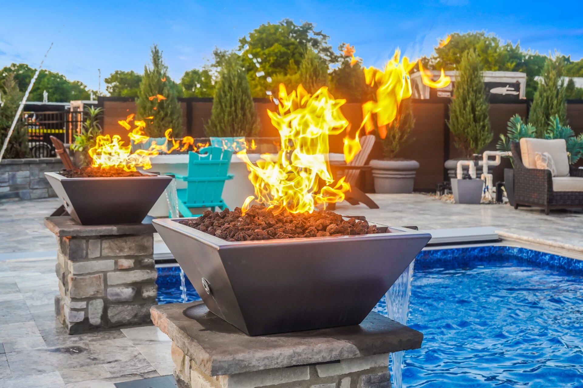 Backyard pool with two stone fire bowls burning near blue water and patio seating