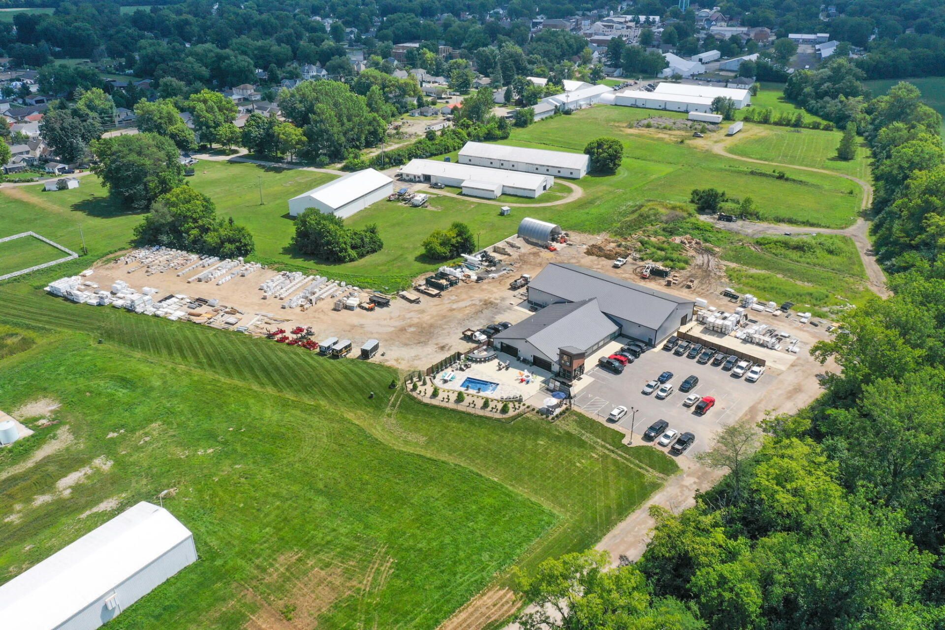 Aerial view of a construction site with parked vehicles, green fields, and surrounding trees