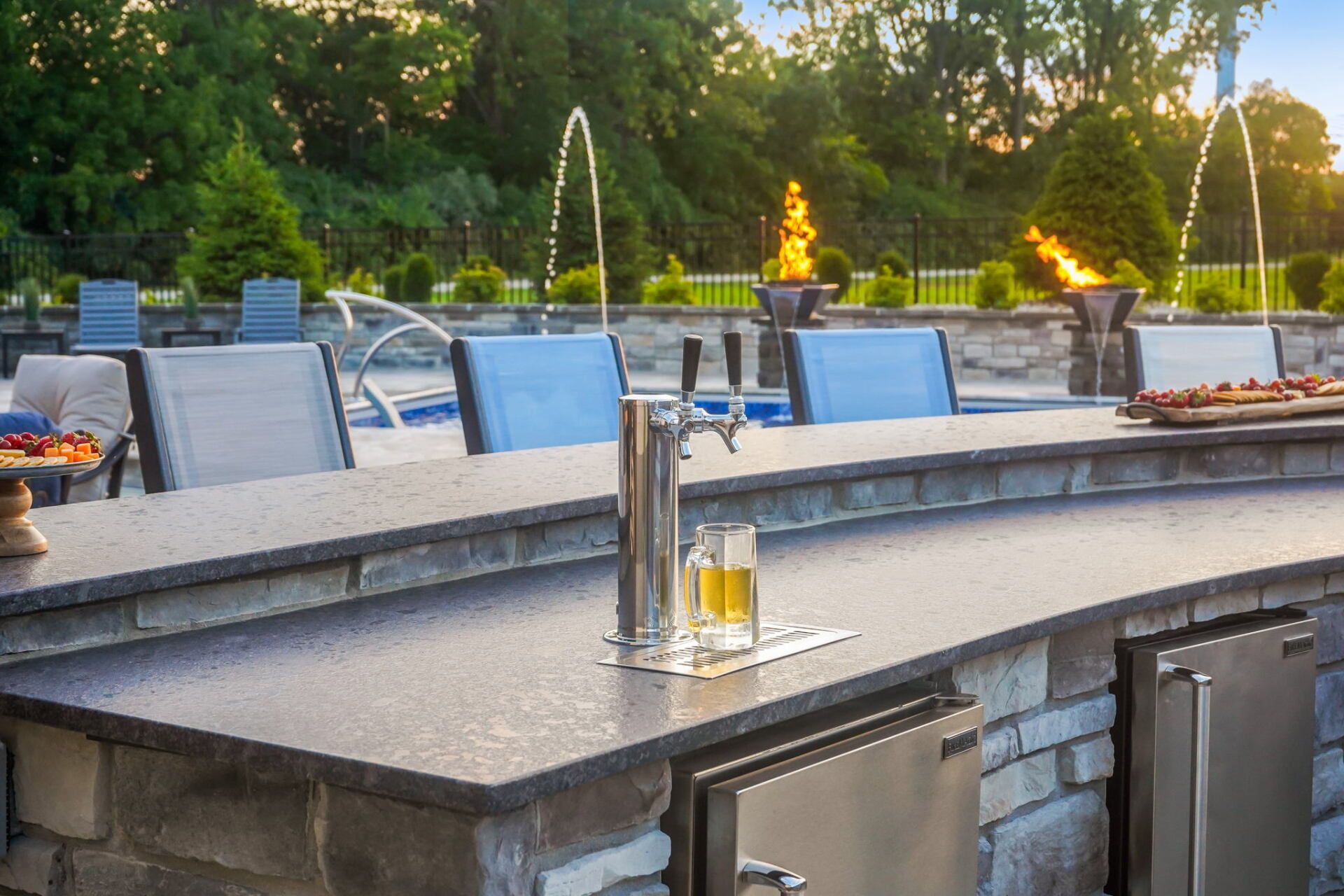 Outdoor patio with stone bar, chairs, drinks, and a fountain in the background