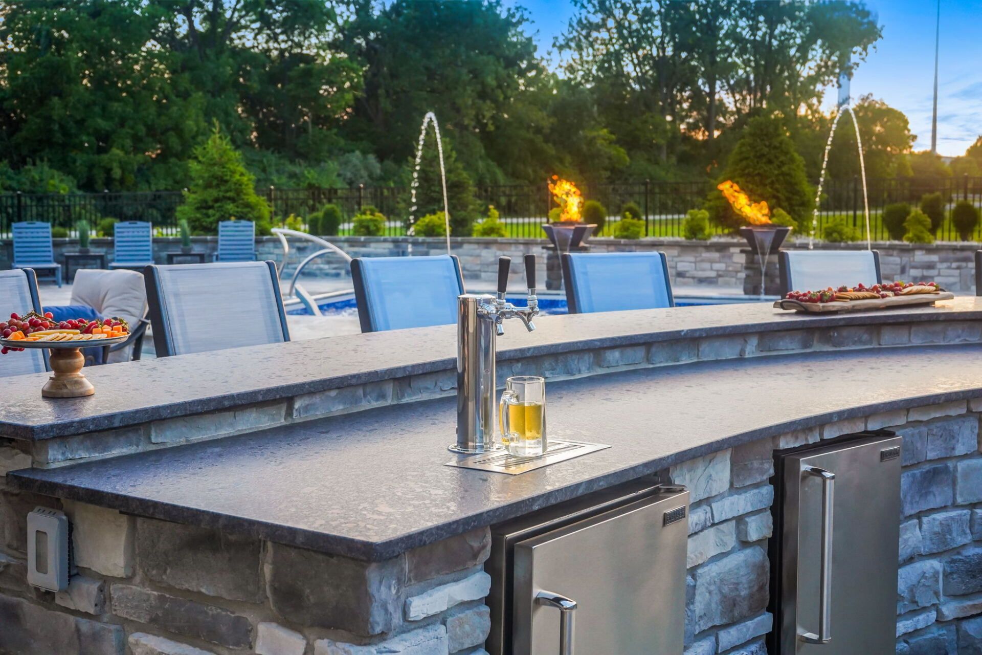 Outdoor patio with blue chairs, stone tables, and fire pits in a landscaped garden at dusk