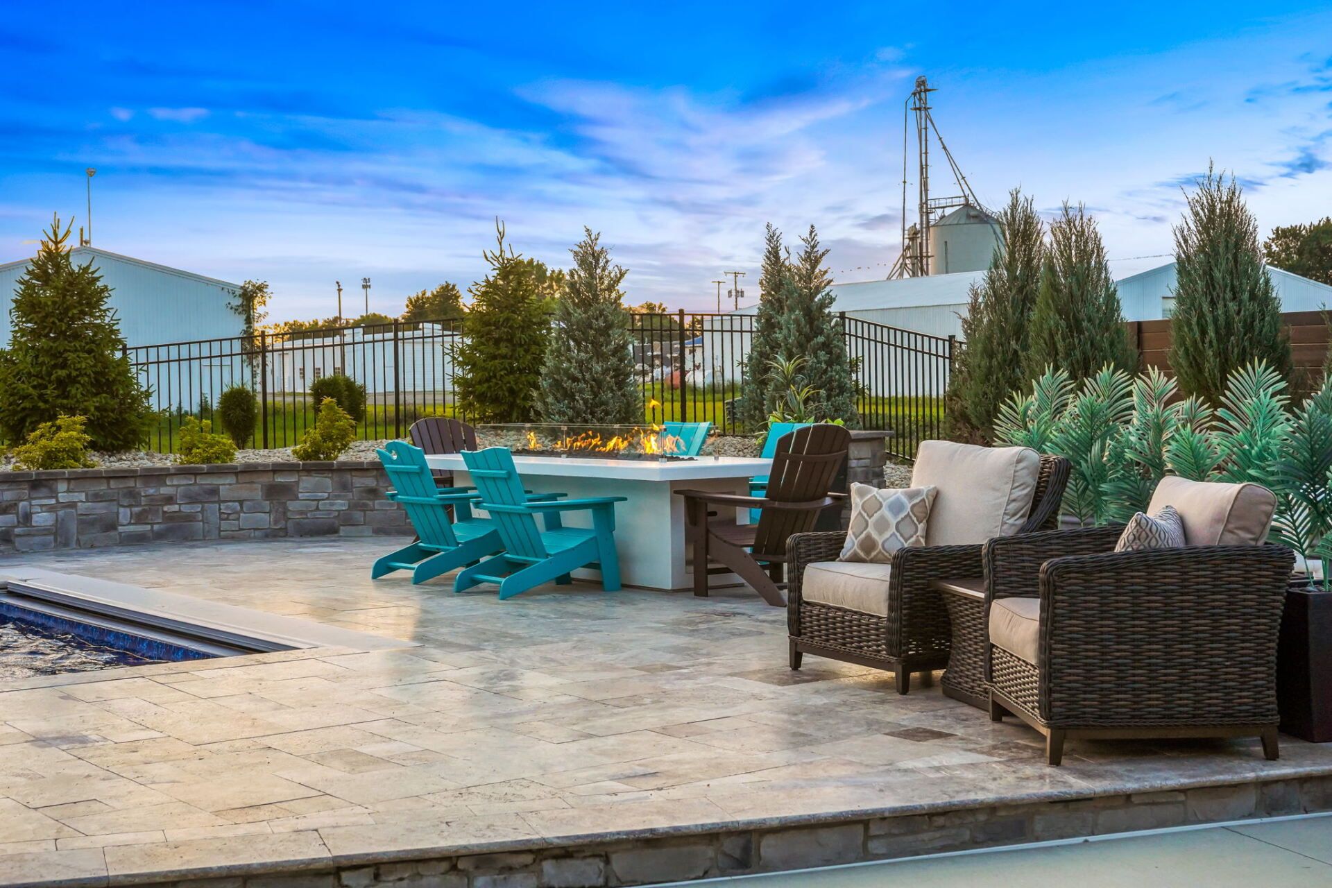 Patio with wicker seating, turquoise chairs, and a pool under a bright sky