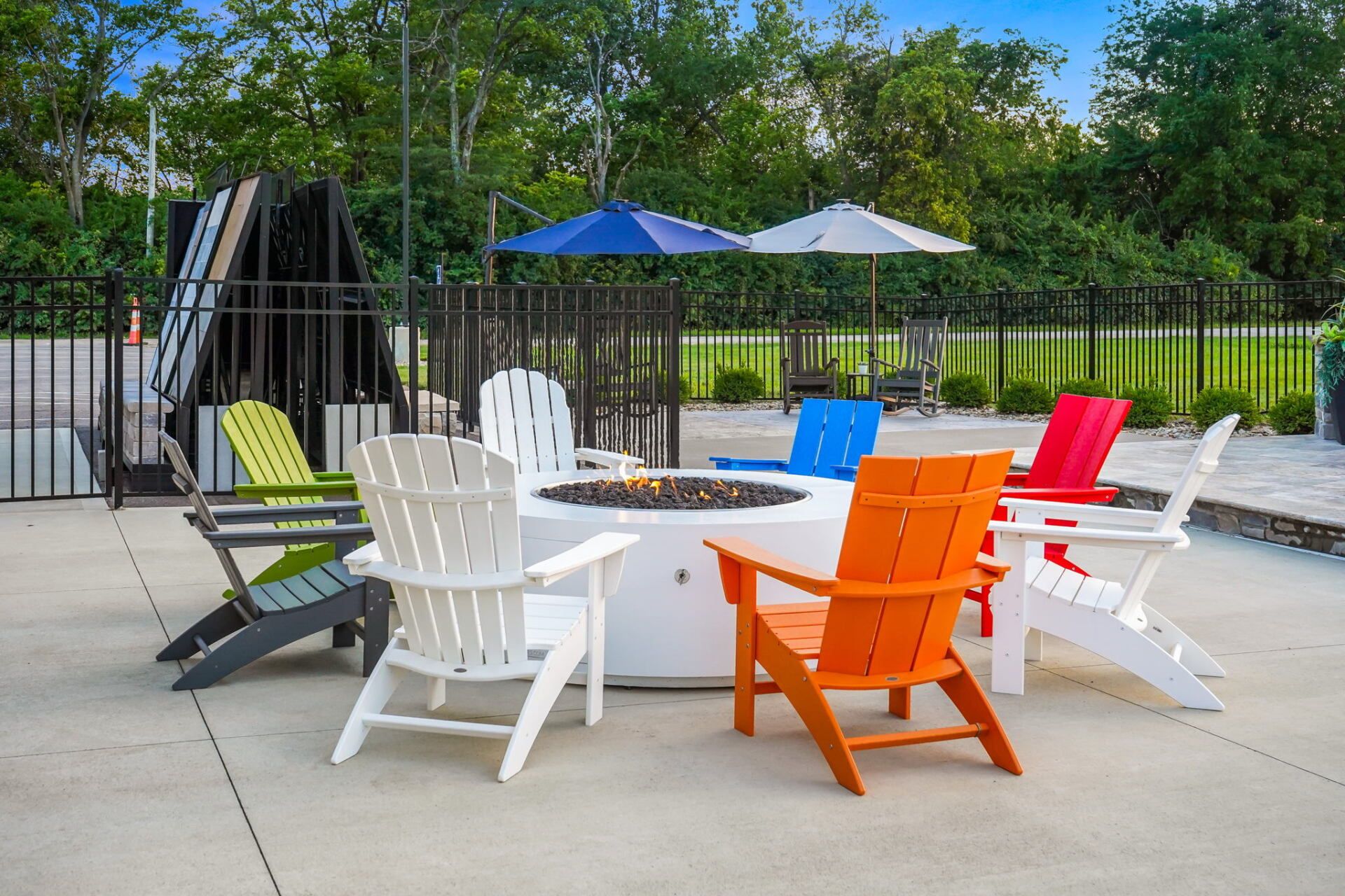 Colorful Adirondack chairs around a fire pit on a patio, with umbrellas and a swing chair nearby.