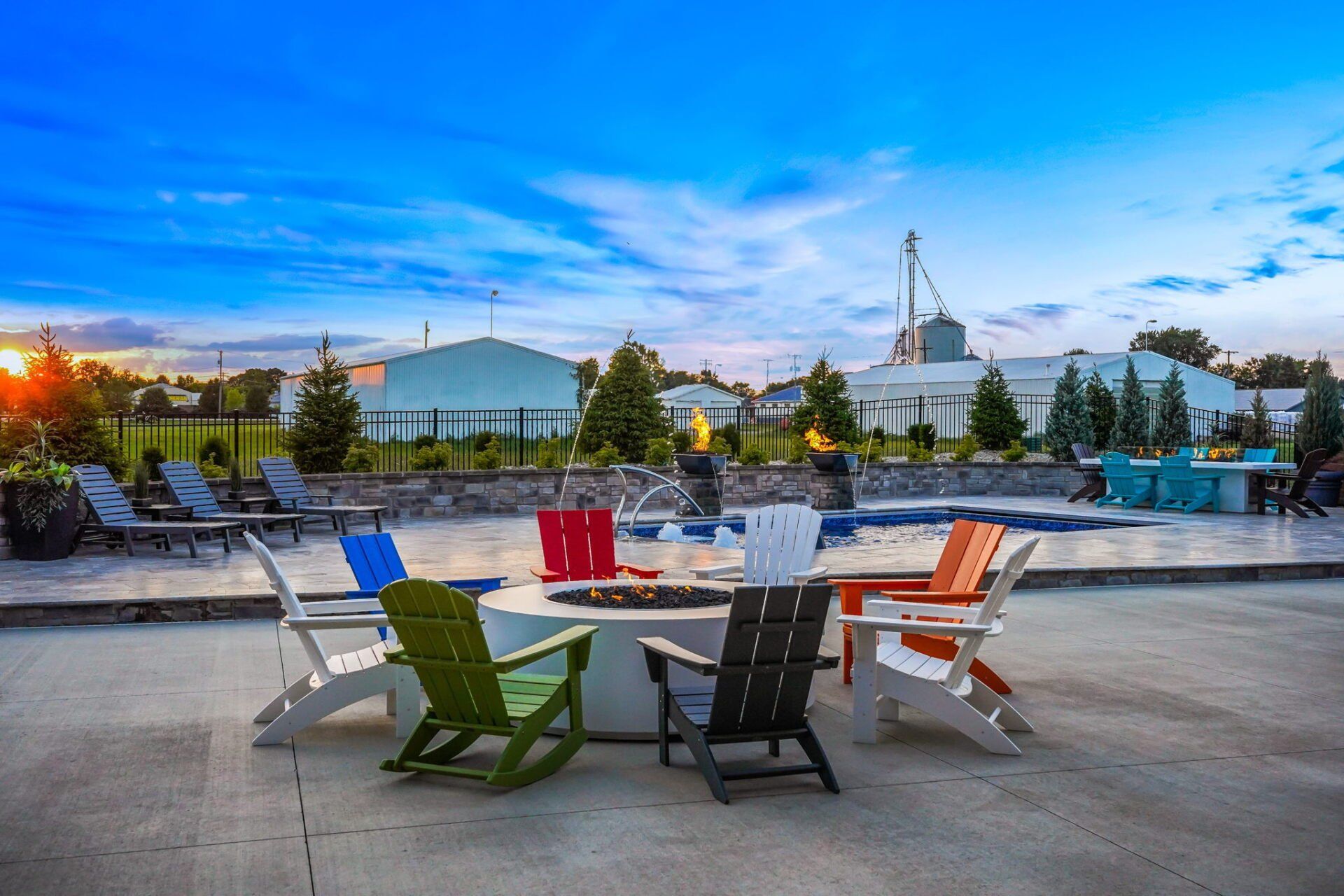 Outdoor rooftop lounge with colorful chairs around a fire pit at sunset.