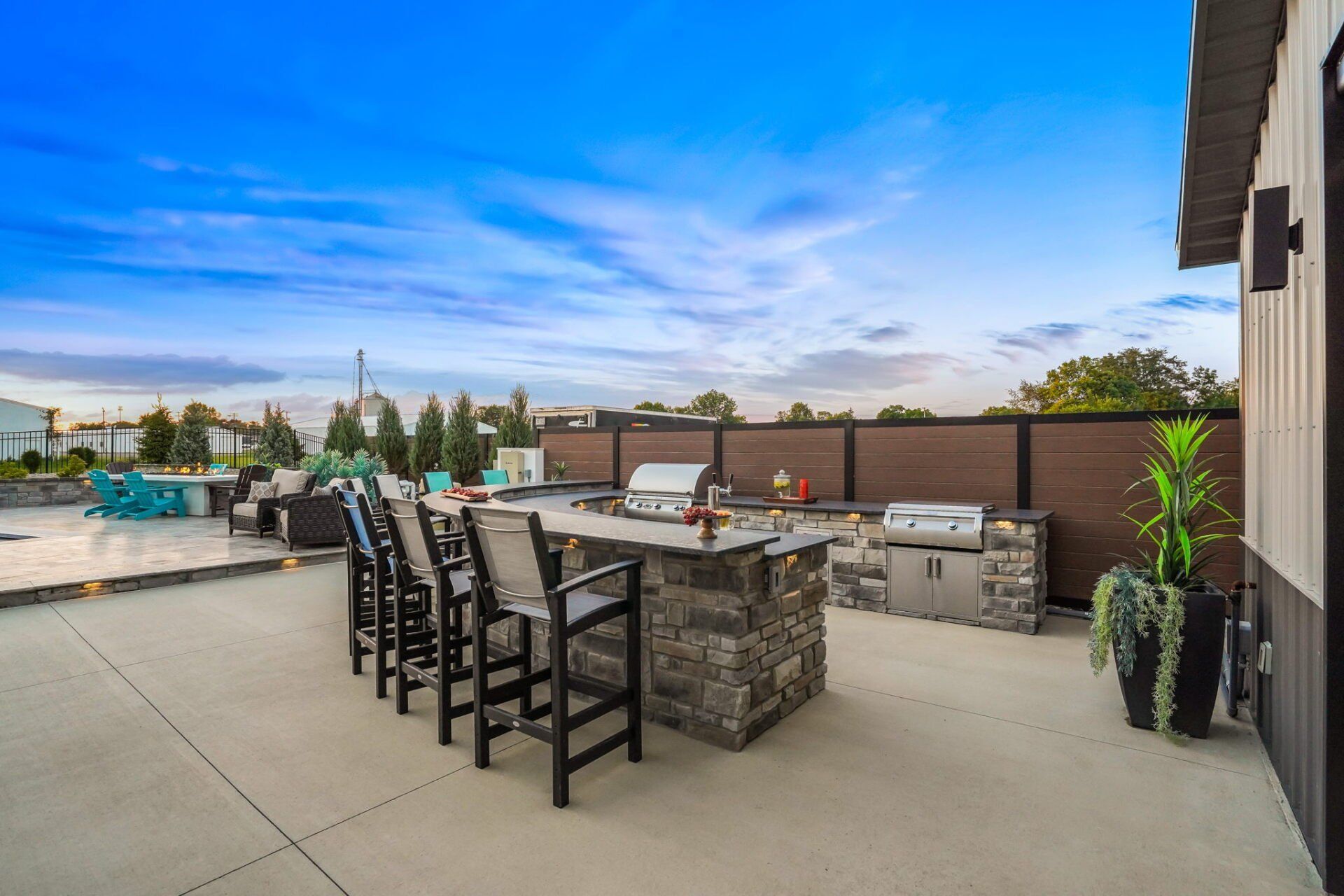 Backyard patio with stone bar seating, outdoor dining chairs, and a view of the pool and sky