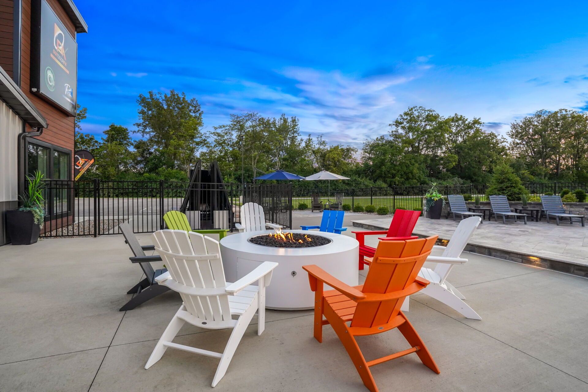 Outdoor patio with white and orange chairs around a fire pit on a sunny day