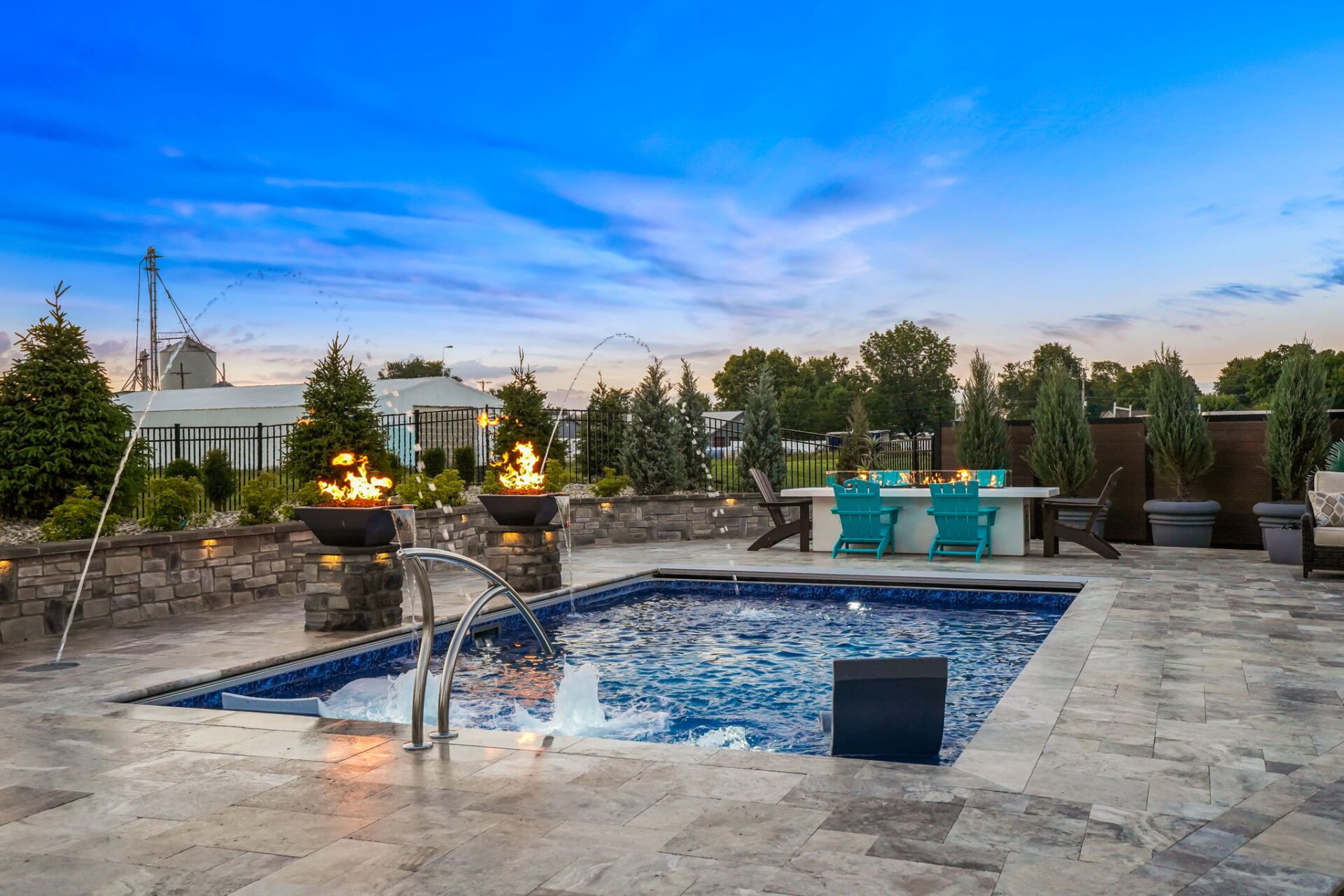 Patio with fire pits, pool, turquoise seating, and potted plants at dusk