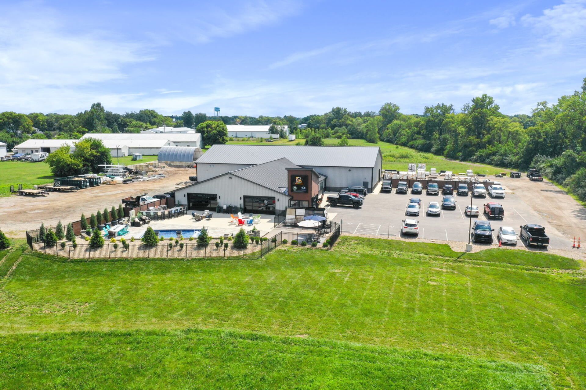 Aerial view of a farm market with a parking lot, greenhouse, and grassy fields under a blue sky