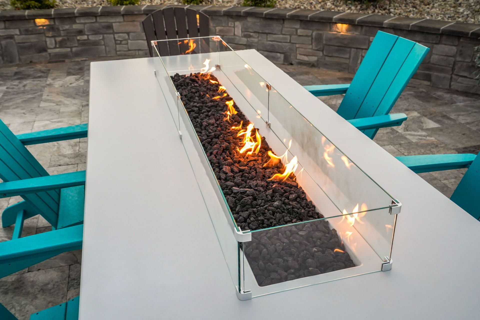 Modern outdoor fire pit on a white table, with turquoise chairs around it